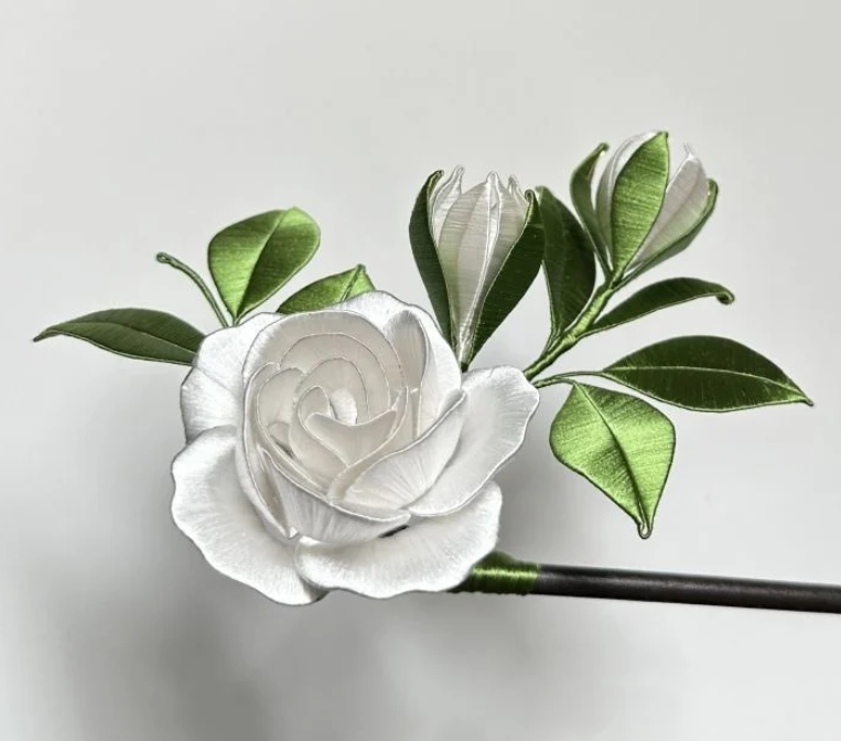 A decorative artificial white rose with green leaves on a white background.