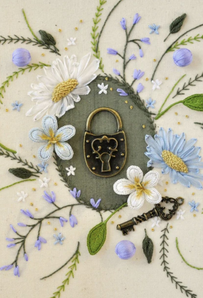 Embroidery art featuring embroidered flowers, leaves, and small decorative yellow dots surrounding a vintage brass lock with a heart-shaped keyhole, and a vintage brass key.