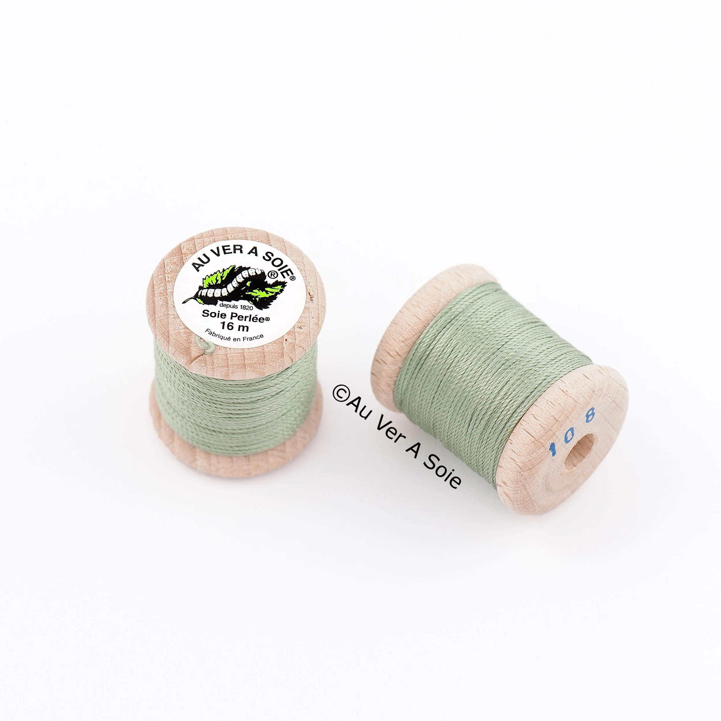 Several wooden spools of thread in pastel colors, including green and beige, placed on a white background.
