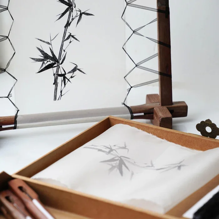 A traditional Japanese paper-making process with a bamboo screen, a wooden frame, and a tray filled with wet paper pulp, producing handmade paper with bamboo leaf shadows.