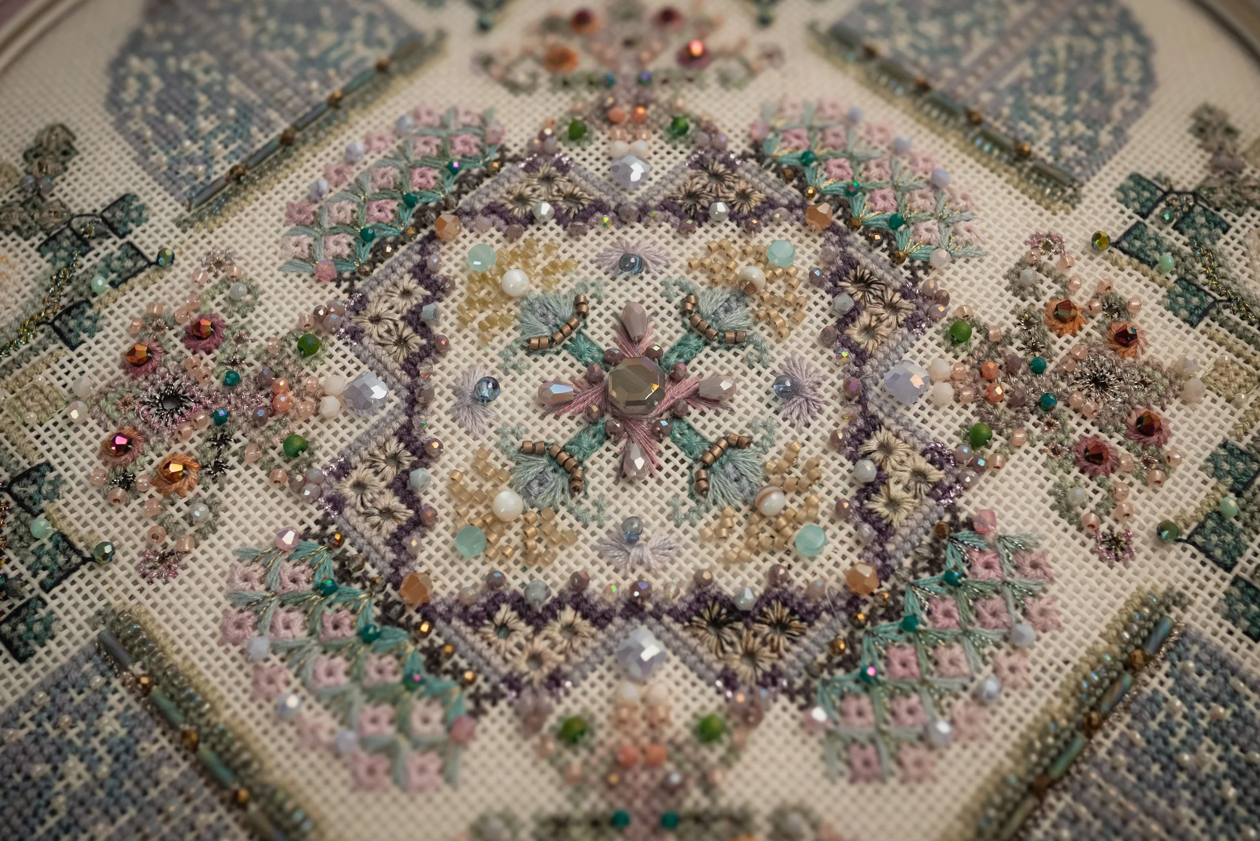 Close-up of a detailed, colorful, embroidered fabric with beads and sequins forming intricate patterns.