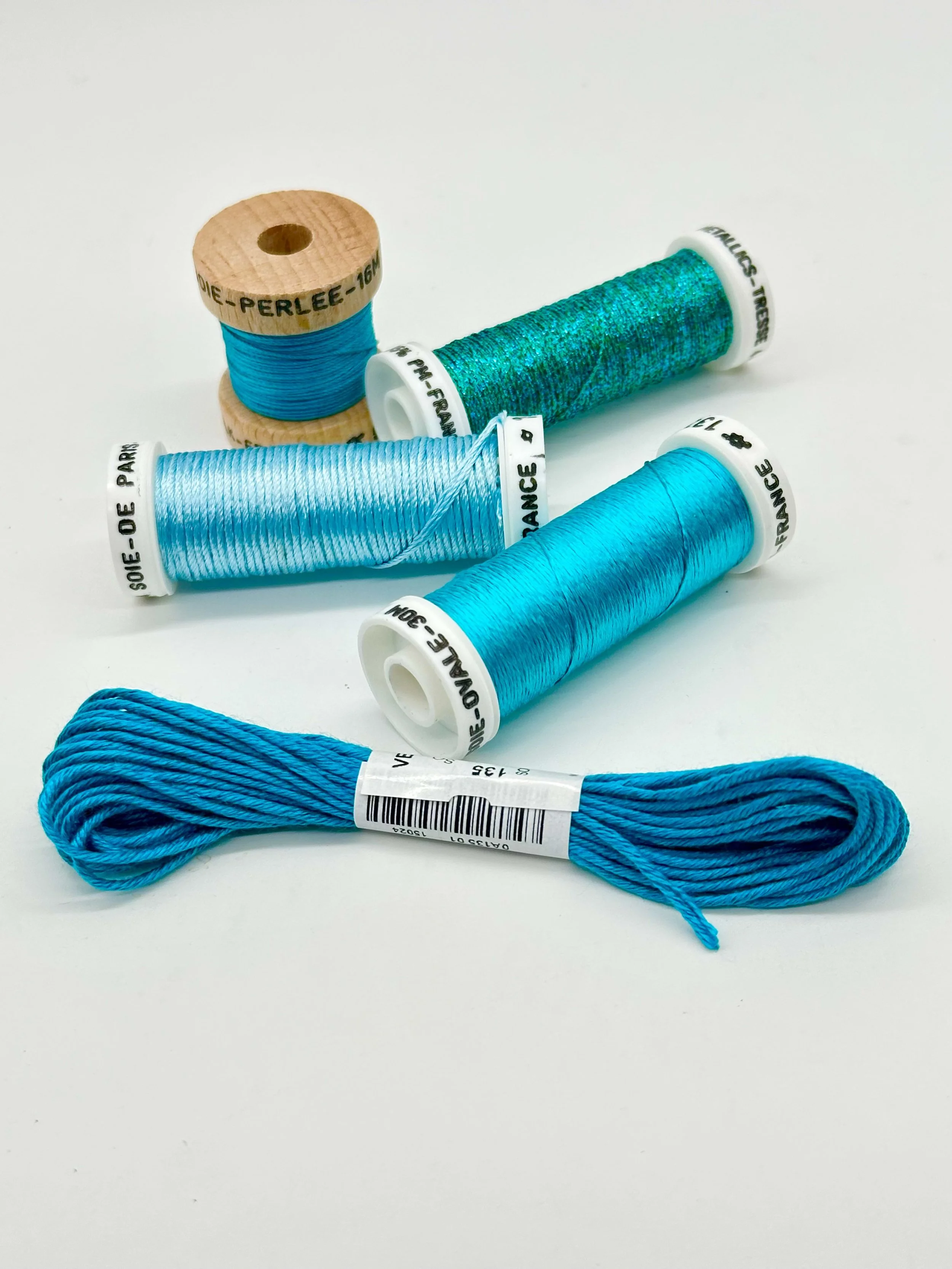 Three spools of blue thread or embroidery floss and one skein of blue thread on a white background.