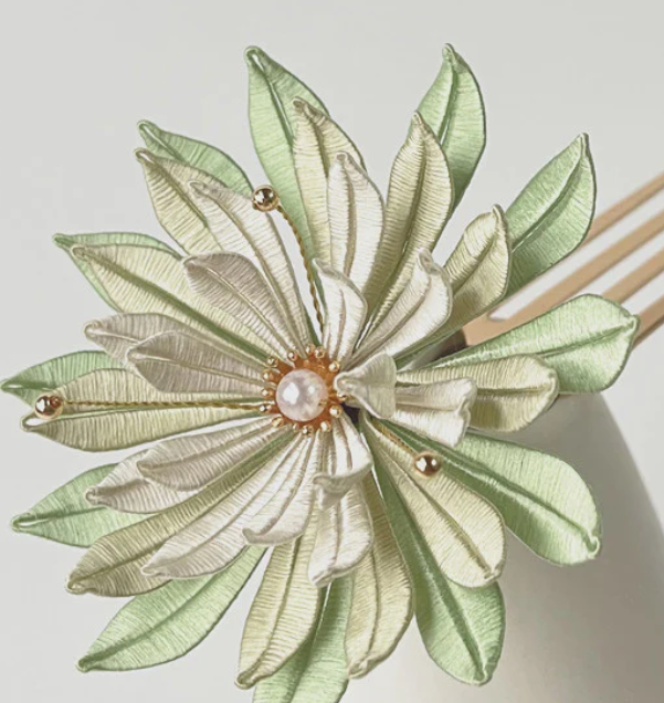 Decorative hair clip with fabric flower design in shades of green and cream, accented with small gold beads and a pearl at the center.