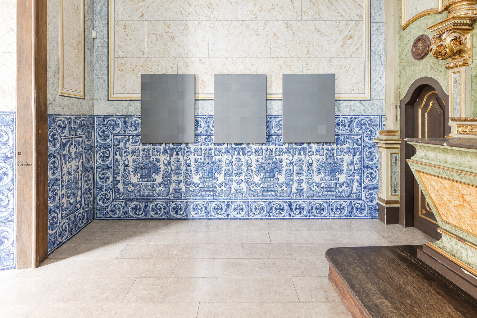 Interior view of a room with blue and white decorative tiled walls, three gray rectangular panels on the wall, and ornate gold and dark wood architectural details.
