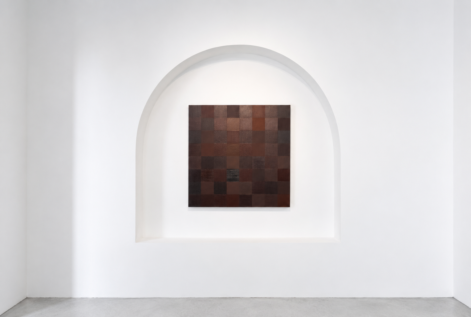 A dark brown mosaic art piece composed of small square tiles, hung on a white wall within a recessed arch.