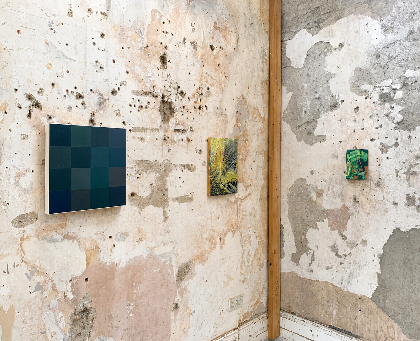 Gallery wall with three small modern paintings on a distressed, textured wall in an art space.