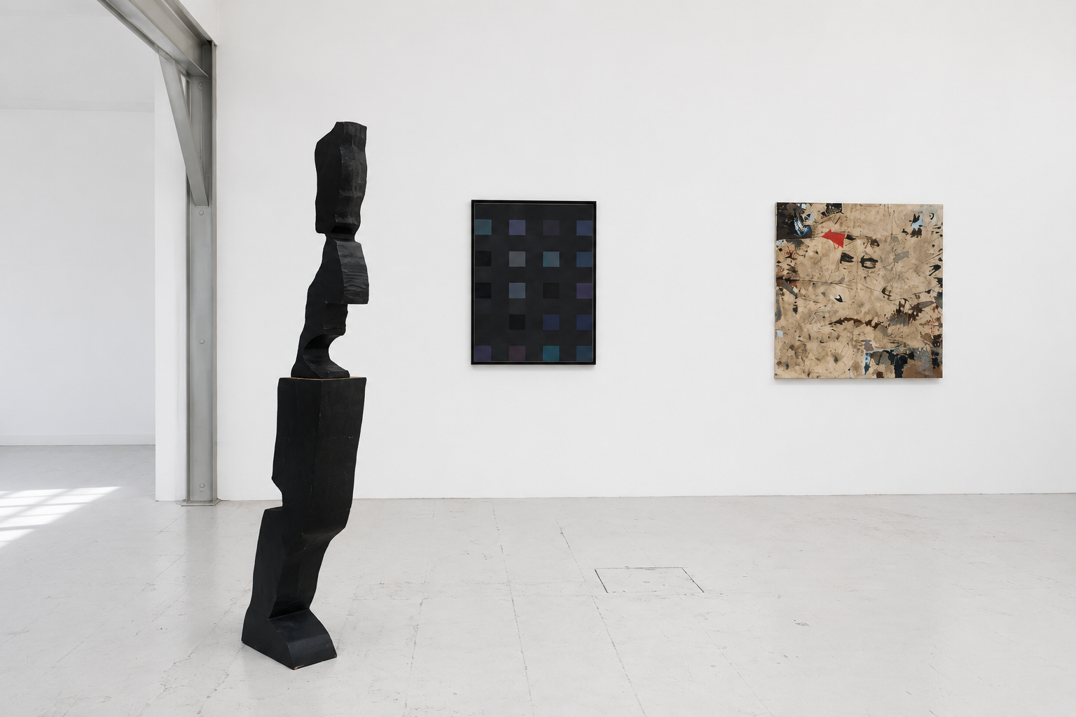 Contemporary art gallery with a black abstract sculpture in the foreground and two framed abstract paintings on a white wall.