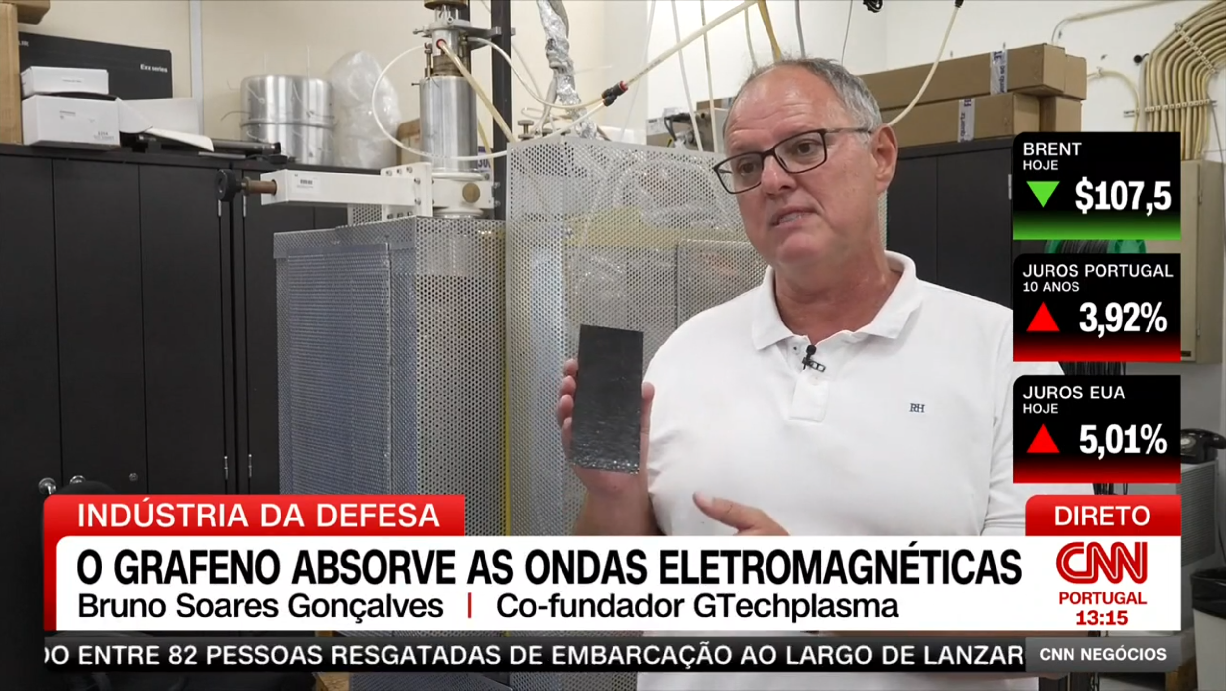 Bruno Soares Gonçalves, co-founder of GTechPlasma, holding a black object, with scientific equipment and electrical wires in the background, on a CNN news broadcast about graphene absorbing electromagnetic waves.