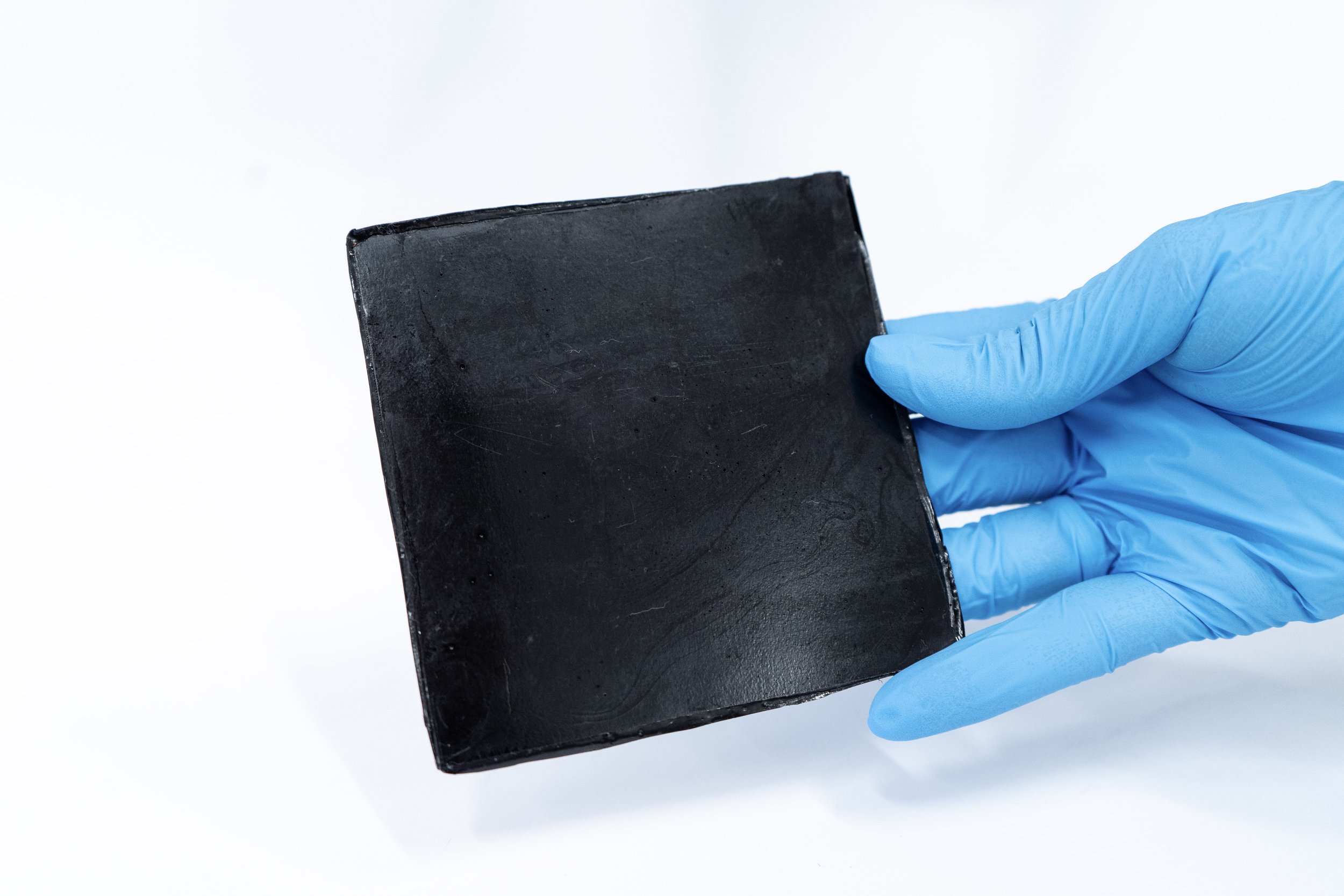 A hand wearing a blue glove holding a black rectangular piece of material against a white background.