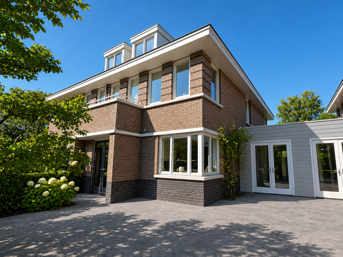 Uitzicht op een modern, hoekwoning met bakstenen gevels en grote ramen, omgeven door bomen op een heldere dag.
