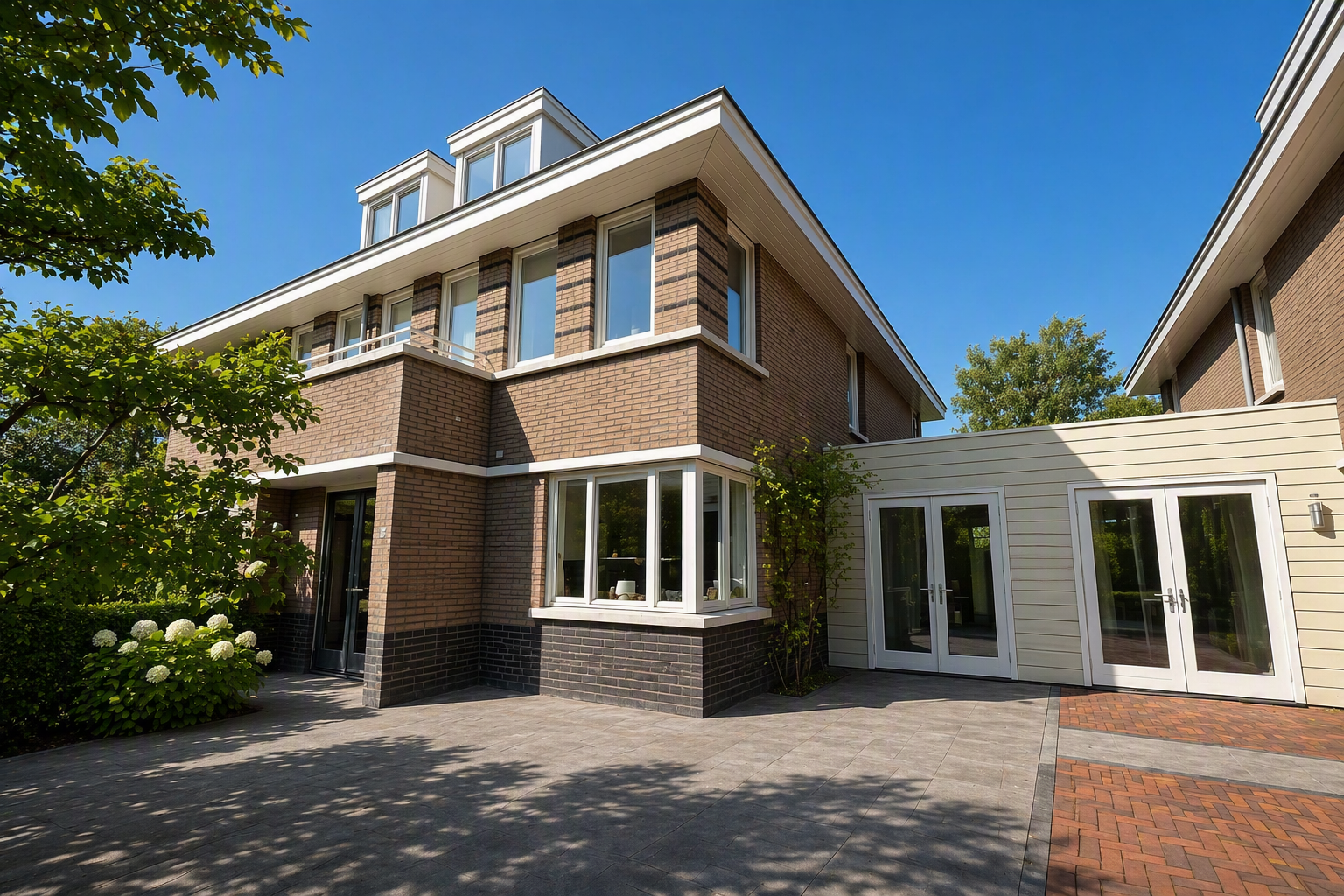 Uitzicht op een modern, hoekwoning met bakstenen gevels en grote ramen, omgeven door bomen op een heldere dag.