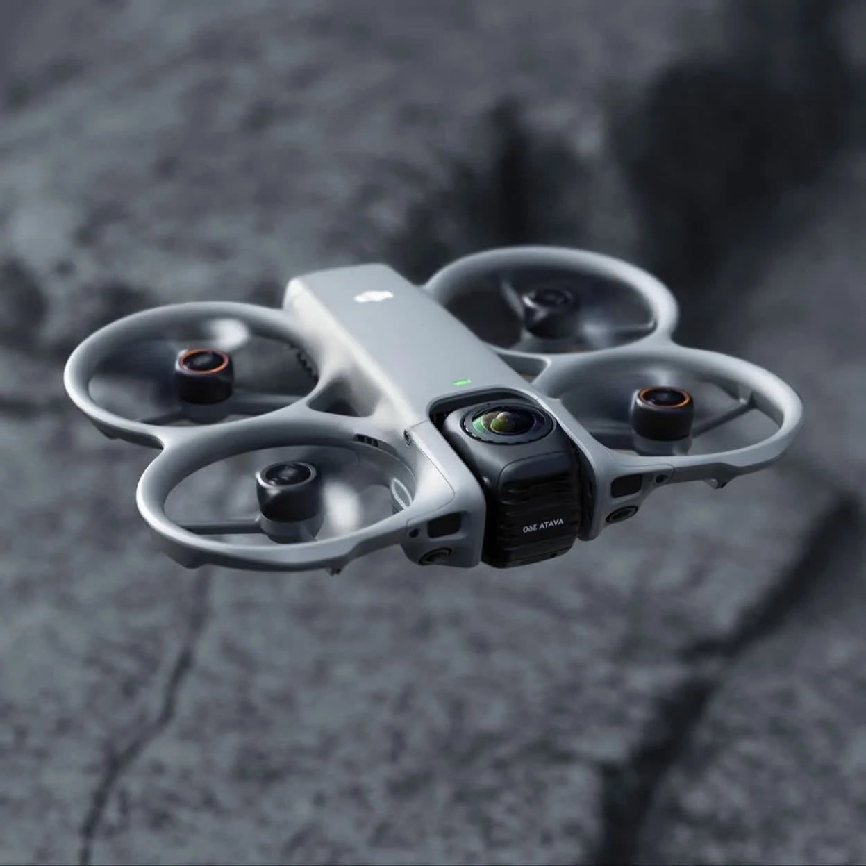 A white quadcopter drone with four propellers flying over a cracked asphalt surface.