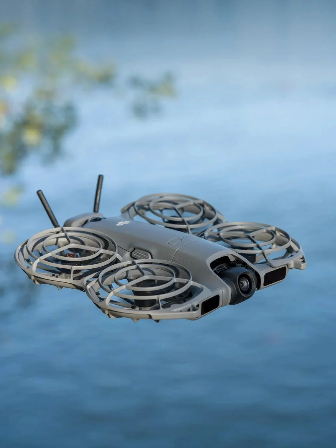 A gray DJI drone with four propellers flying over water.