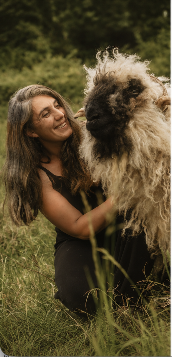 Une femme souriante en noir dans un champ vert, tenant un grand mouton laineux avec un visage noir et des cornes.