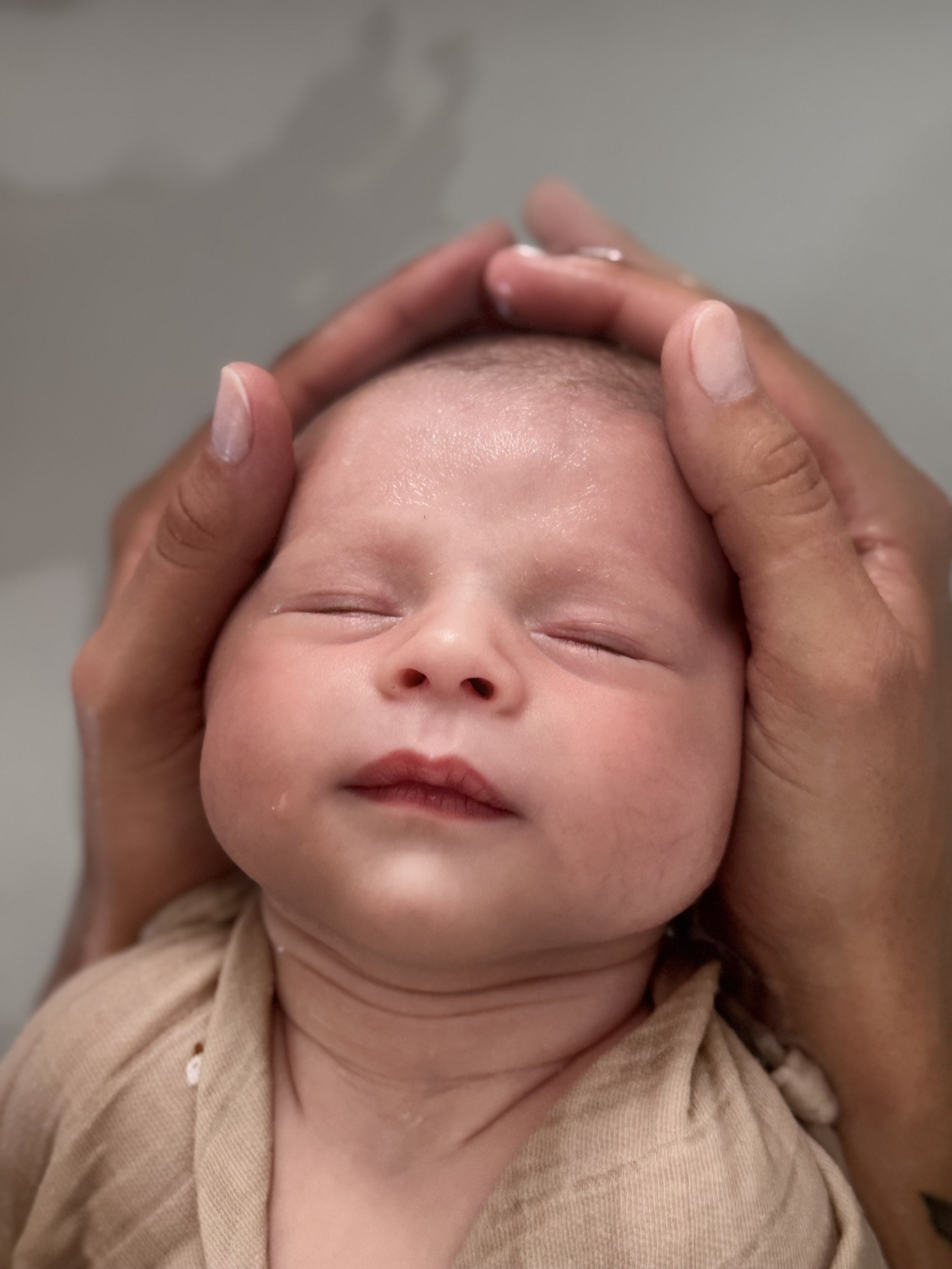 Un bébé qui a les yeux fermés, avec une personne qui lui tient la tête.