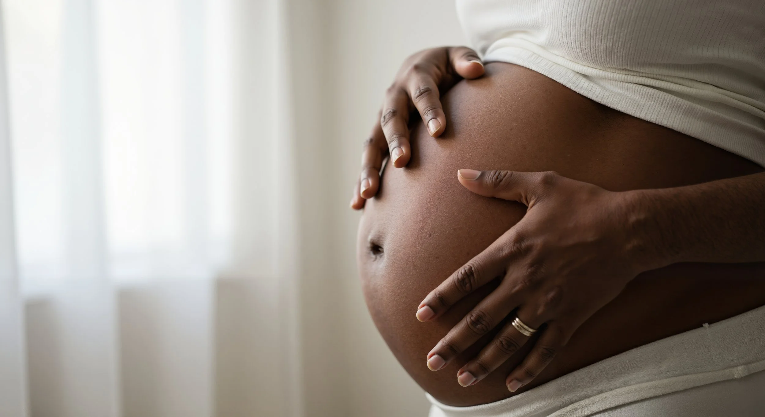 Une personne enceinte qui caresse son ventre, vêtue d'un haut blanc