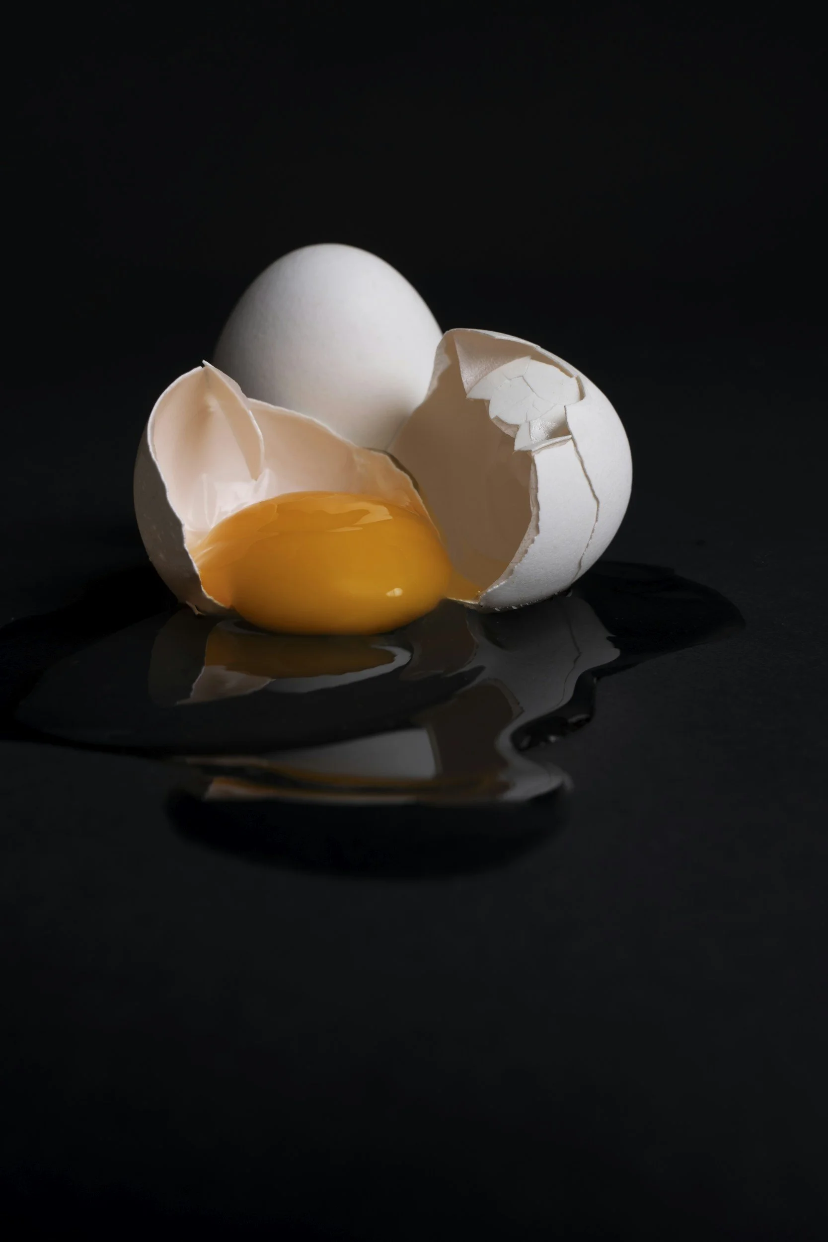 A raw egg with a cracked shell, revealing the yolk and egg white inside, on a dark surface.