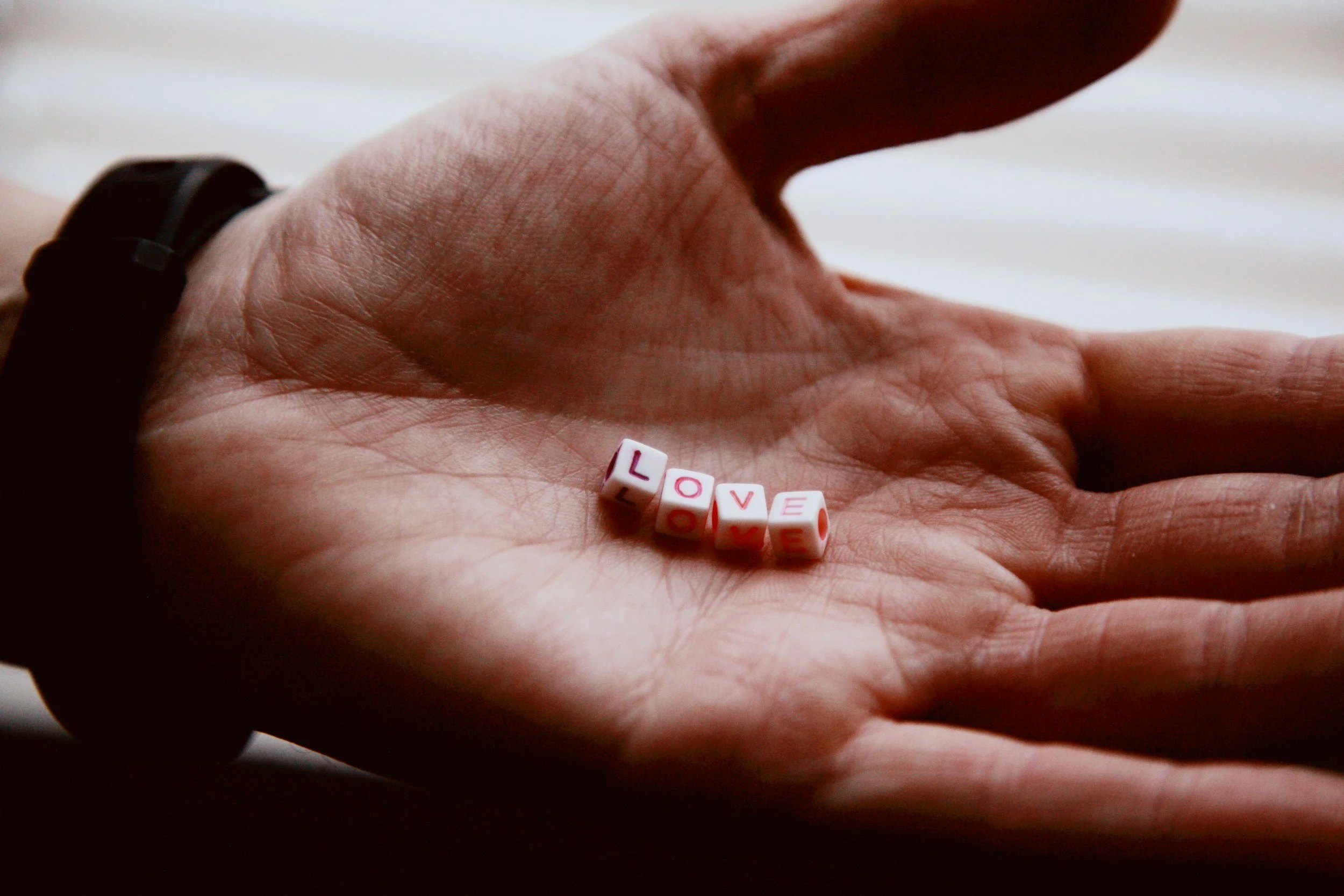 A person's hand holding small pink letter beads spelling the word 'LOVE'.