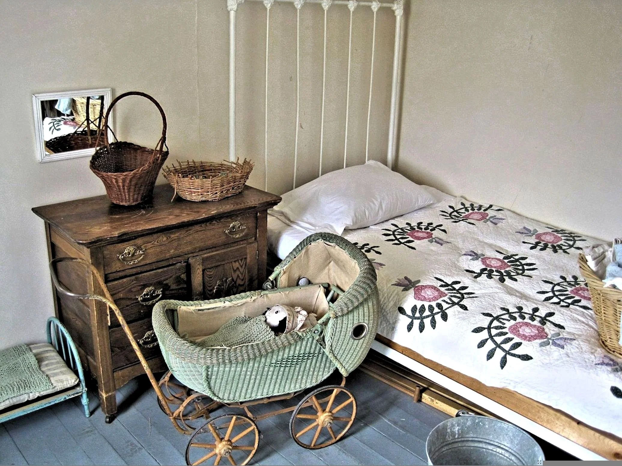Ein Bett mit floral bedruckter Decke, ein alter Holzschrank, mehrere Körbe und ein Kinderwagen im Schlafzimmer.