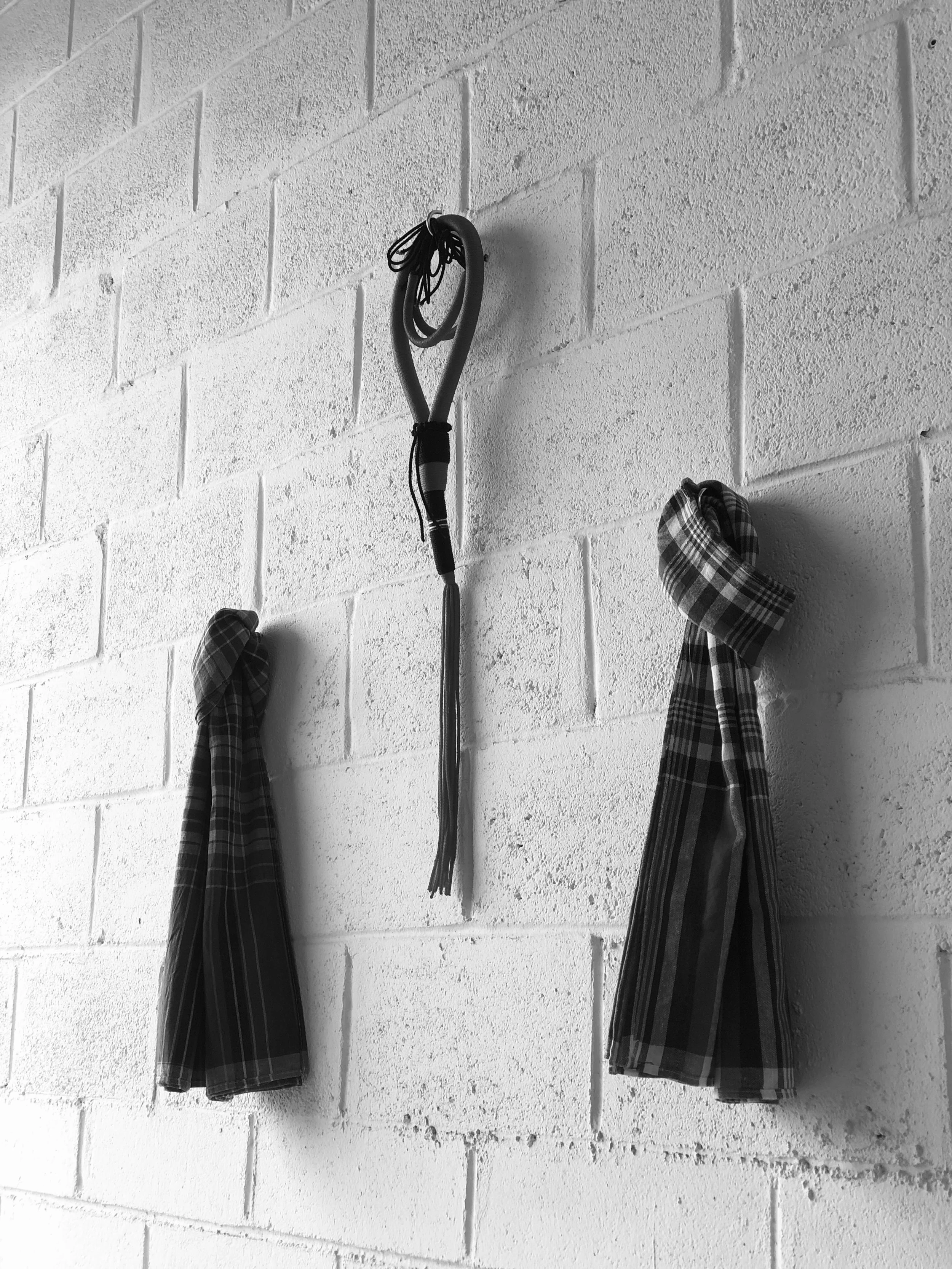 Two plaid shirts hanging on hooks on a white brick wall, with a coiled rope or cable hanging between them.