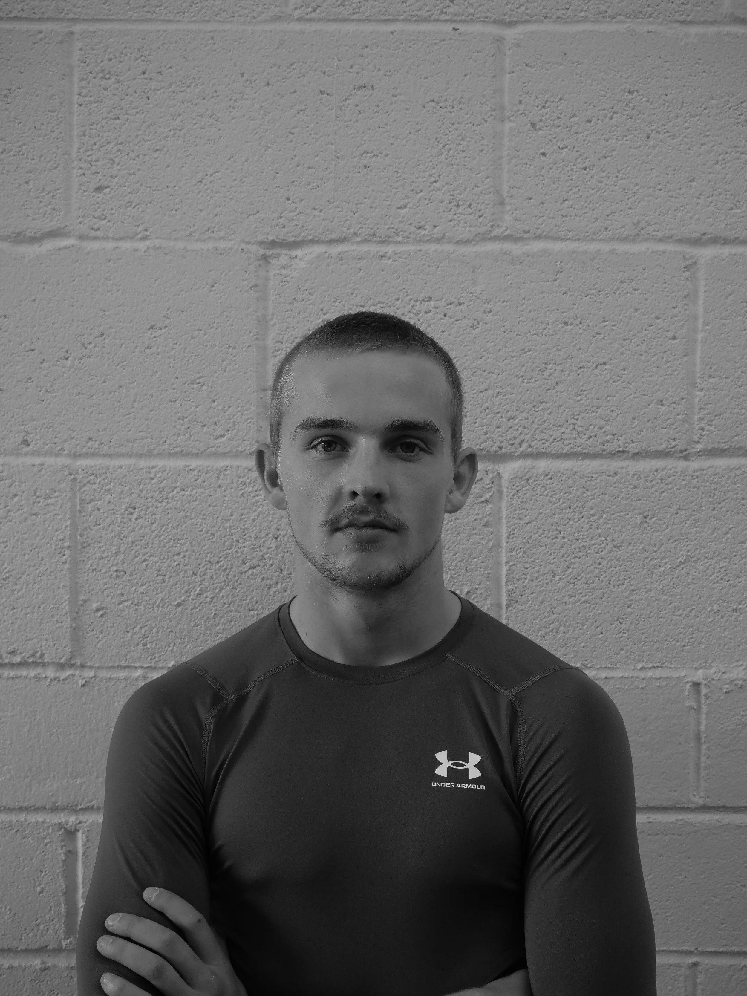 Rufus, Cold Heart MMA Coach, stood against a white brick wall. This photo is in black & white