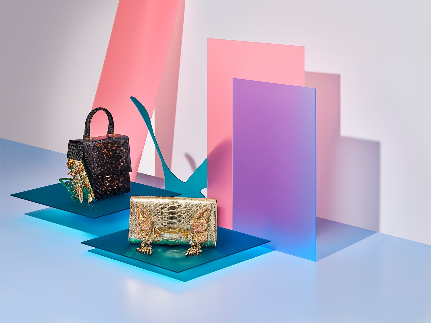 Two decorative handbags displayed on blue platforms with colorful abstract backdrops, including pink, purple, and light gray panels.