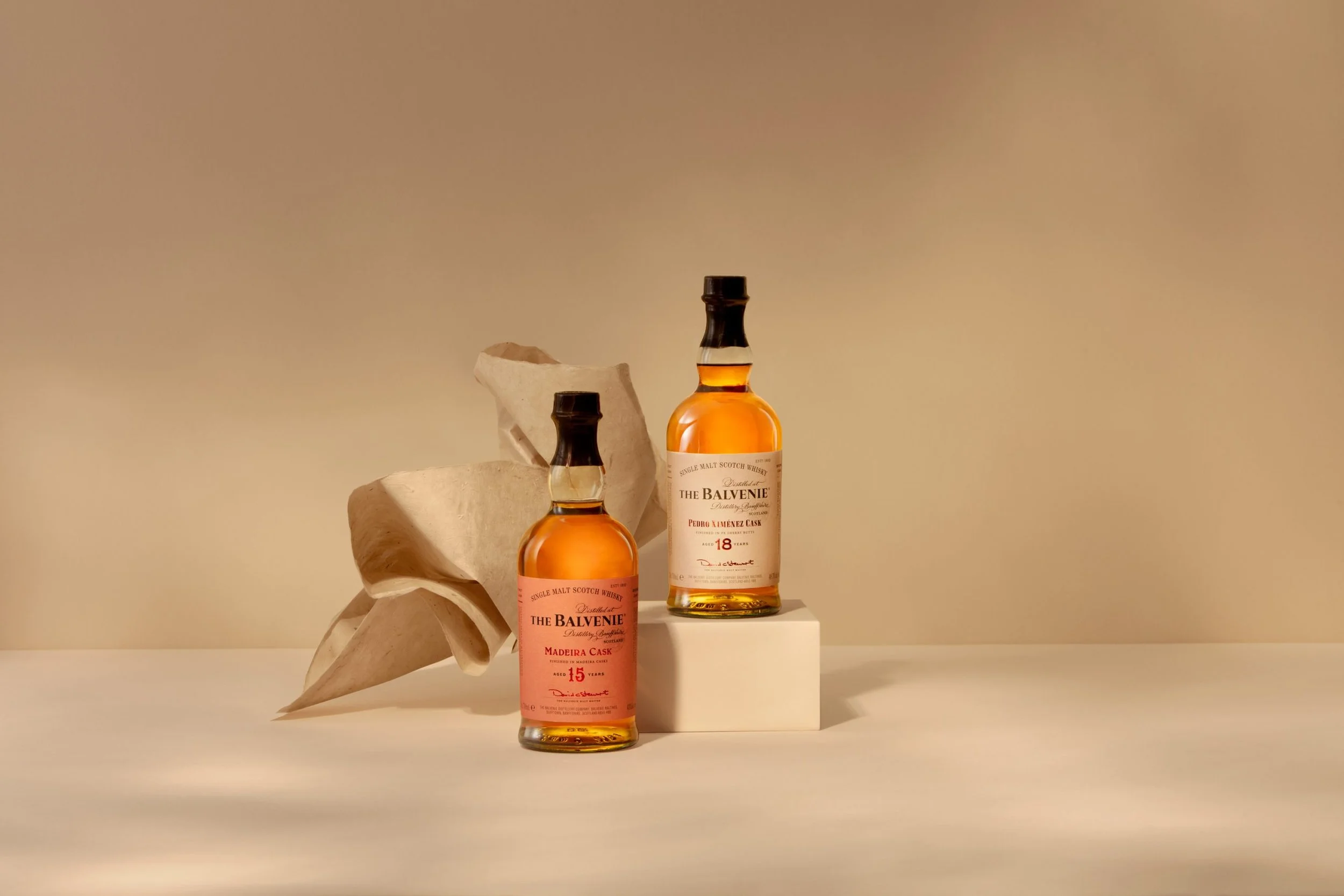 Two bottles of whiskey on display, with a carved stone sculpture and a beige background.