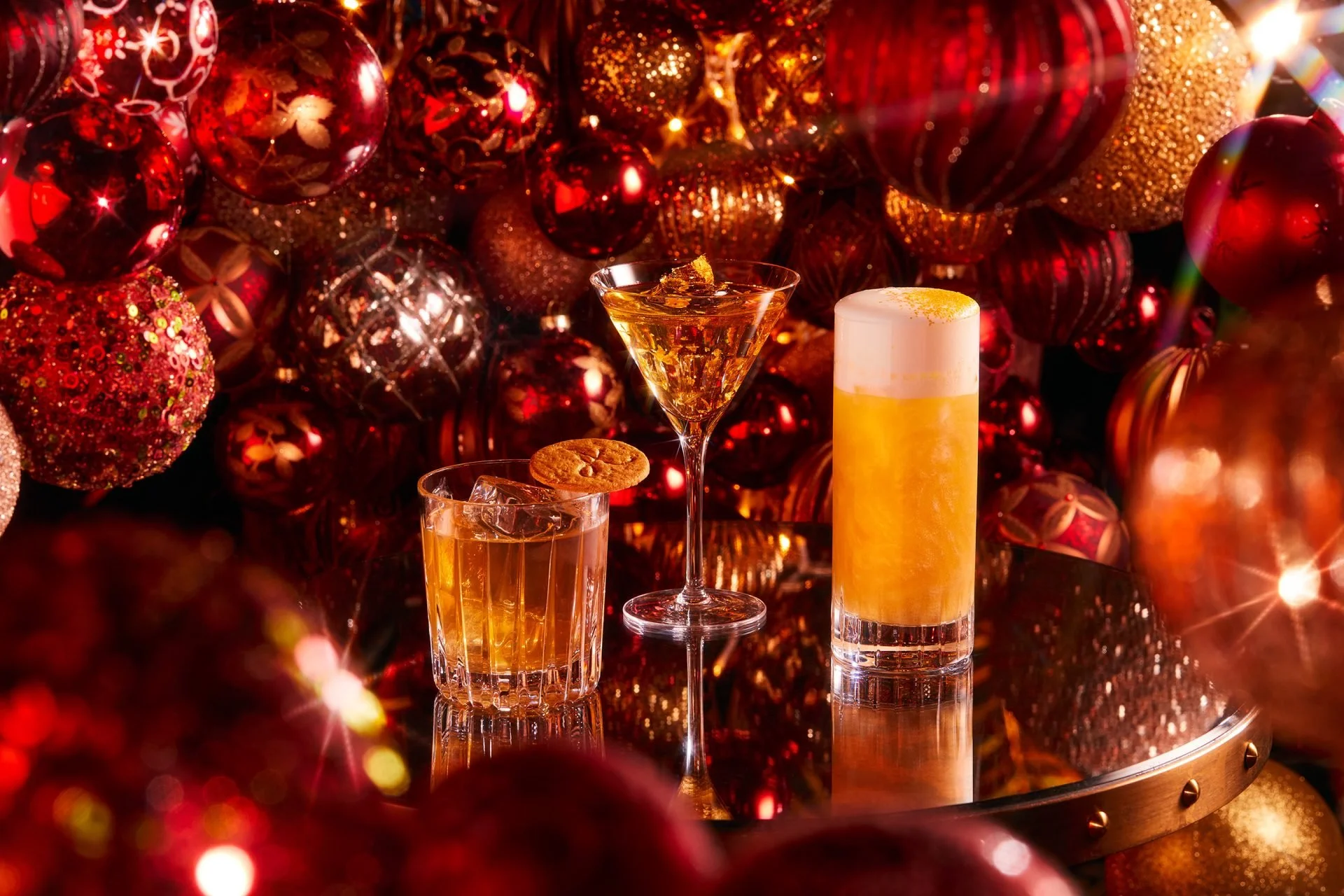 A collection of red and gold Christmas ornaments with two drinks, a cocktail in a martini glass and a beer in a tall glass, surrounded by festive decorations.
