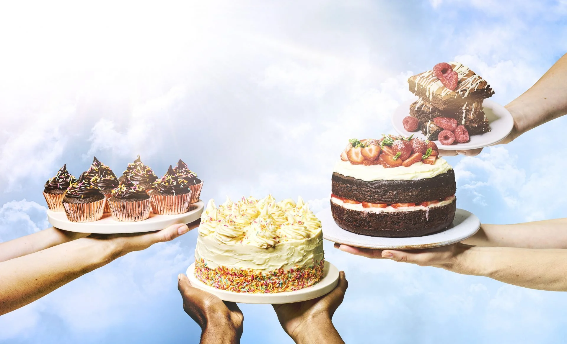 Multiple hands holding plates of assorted cakes and desserts against a cloudy sky background.
