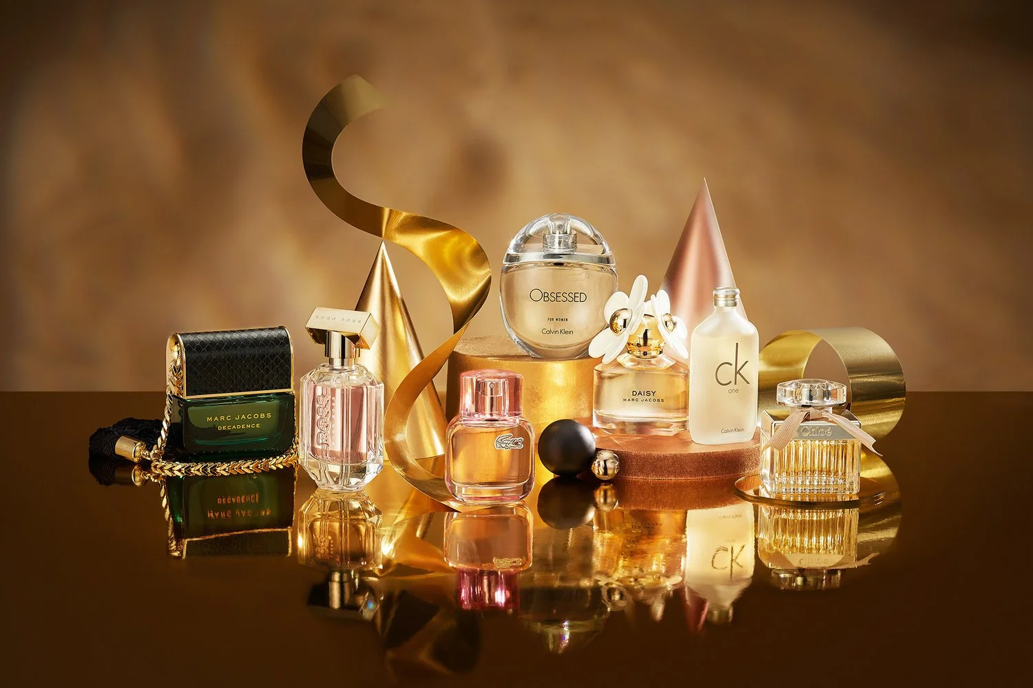 A collection of designer perfume bottles and decorative elements on a gold surface with a warm, reflective background.