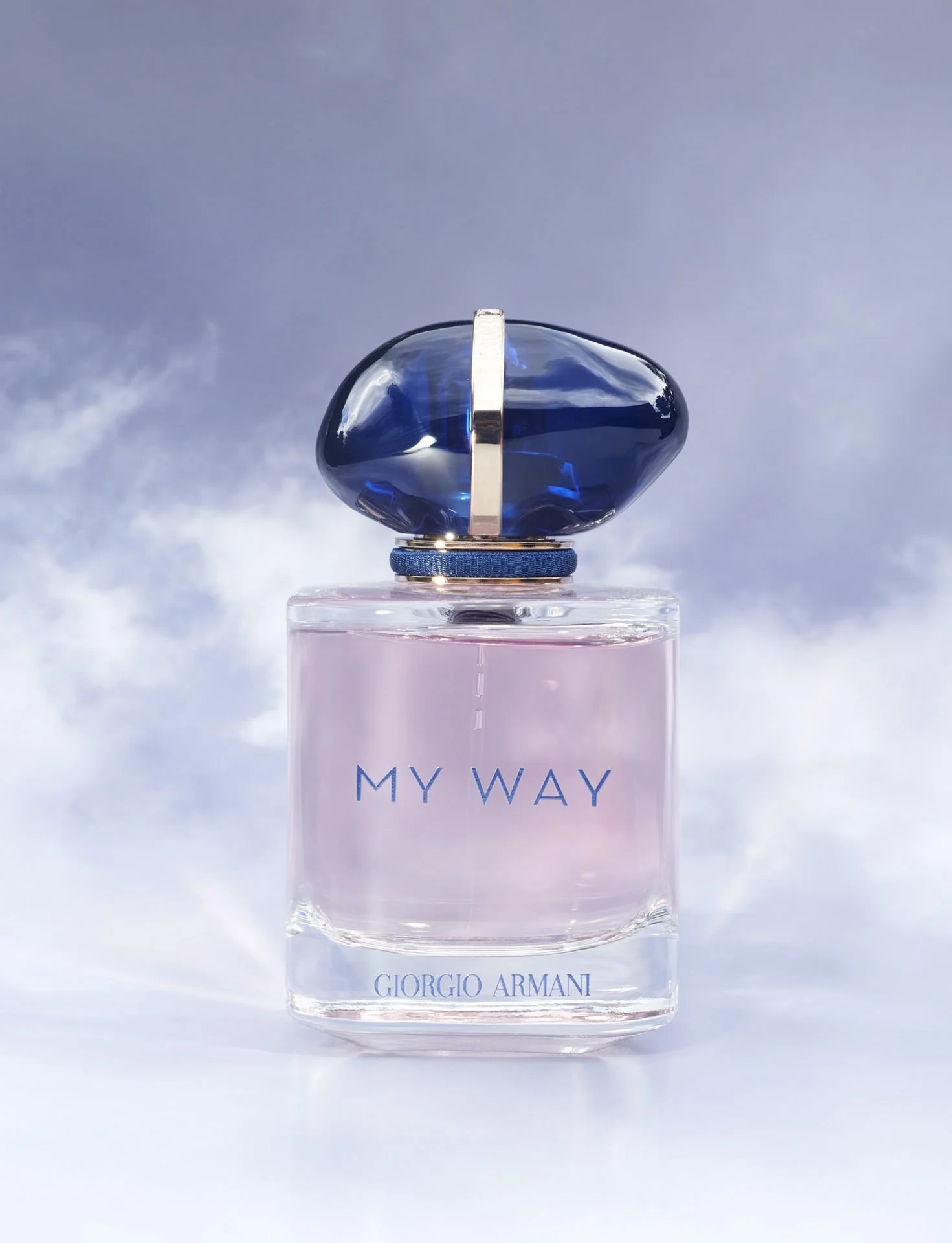 A Giorgio Armani perfume bottle with a clear rectangular base and a rounded, dark blue cap, set against a backdrop of a cloudy sky. The bottle has the words 'MY WAY' and 'GIORGIO ARMANI' printed on it.