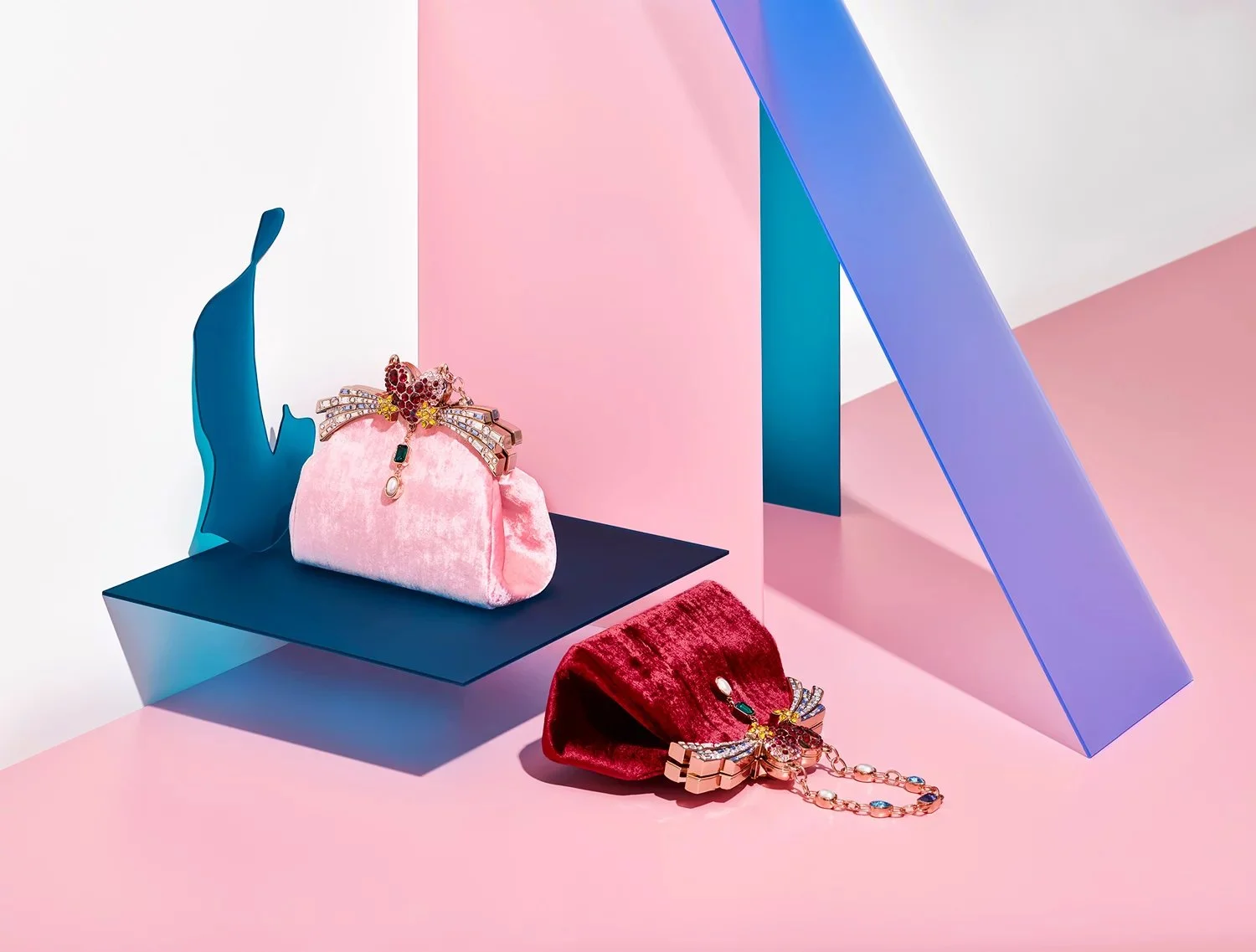 Two velvet handbags, one pink and one red, decorated with jewelry, displayed on lelook, pastel-colored geometric background.