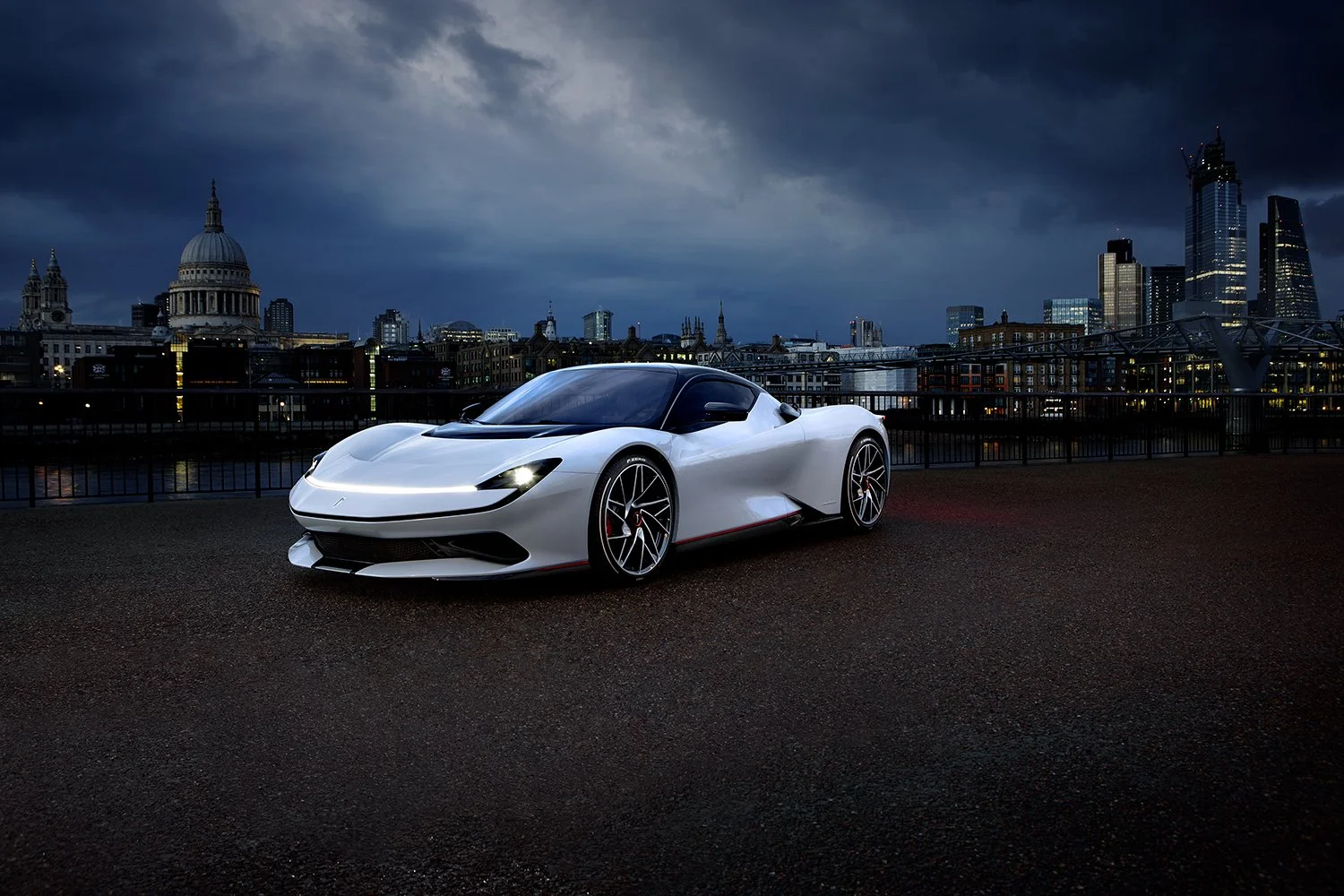 A white sports car parked on a city street at night with a city skyline in the background, including a dome and tall buildings, under a dark cloudy sky.
