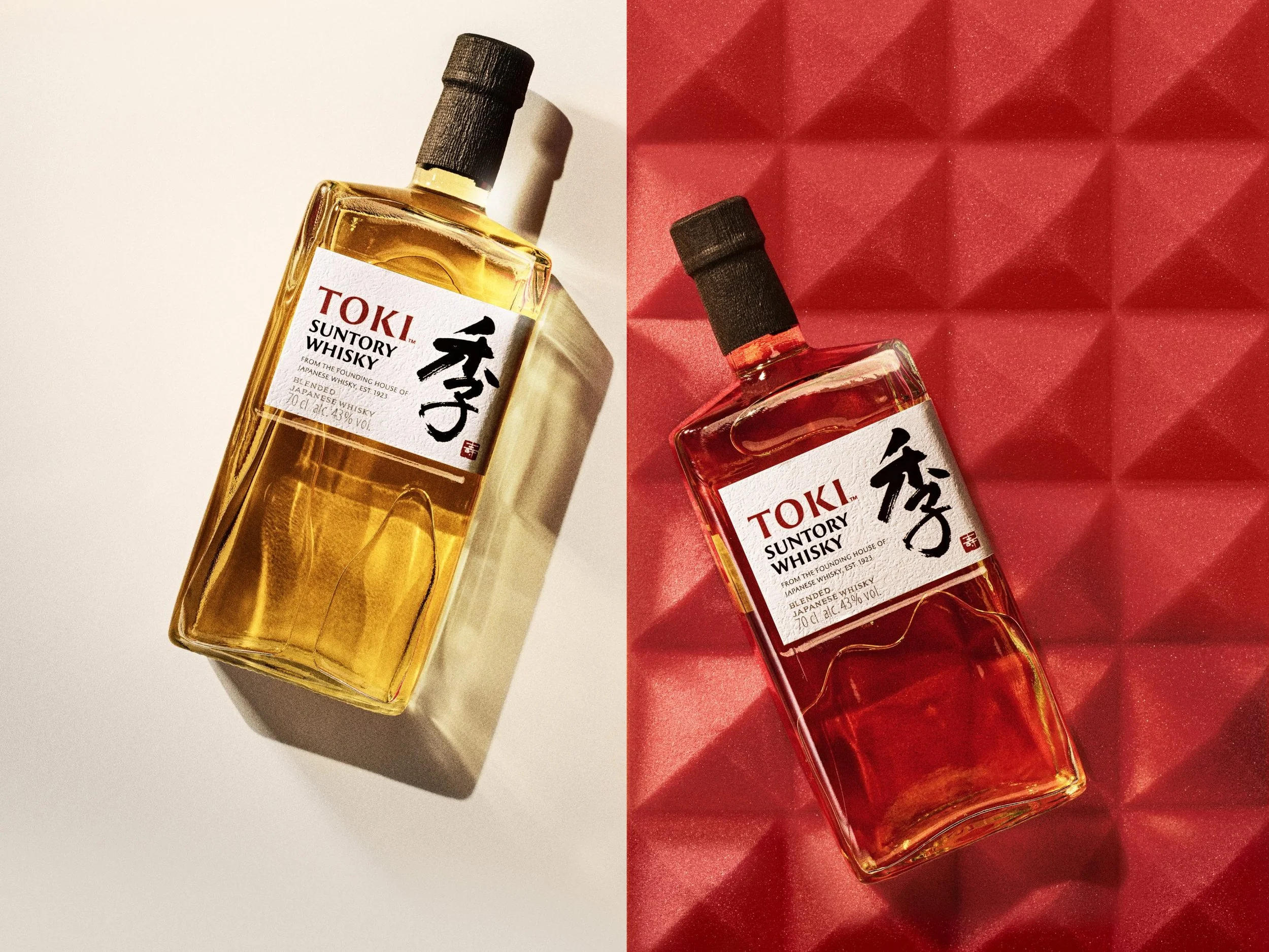Two bottles of TOKI Suntory whisky, one with a golden liquid on the left against a white background, and one with an amber liquid on the right against a red textured background.