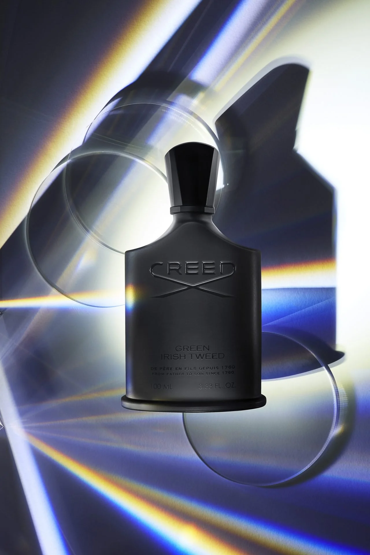 A black bottle labeled 'Creed Green Irish Tweed' placed on reflective, colorful, metallic surfaces with circular disc shapes.