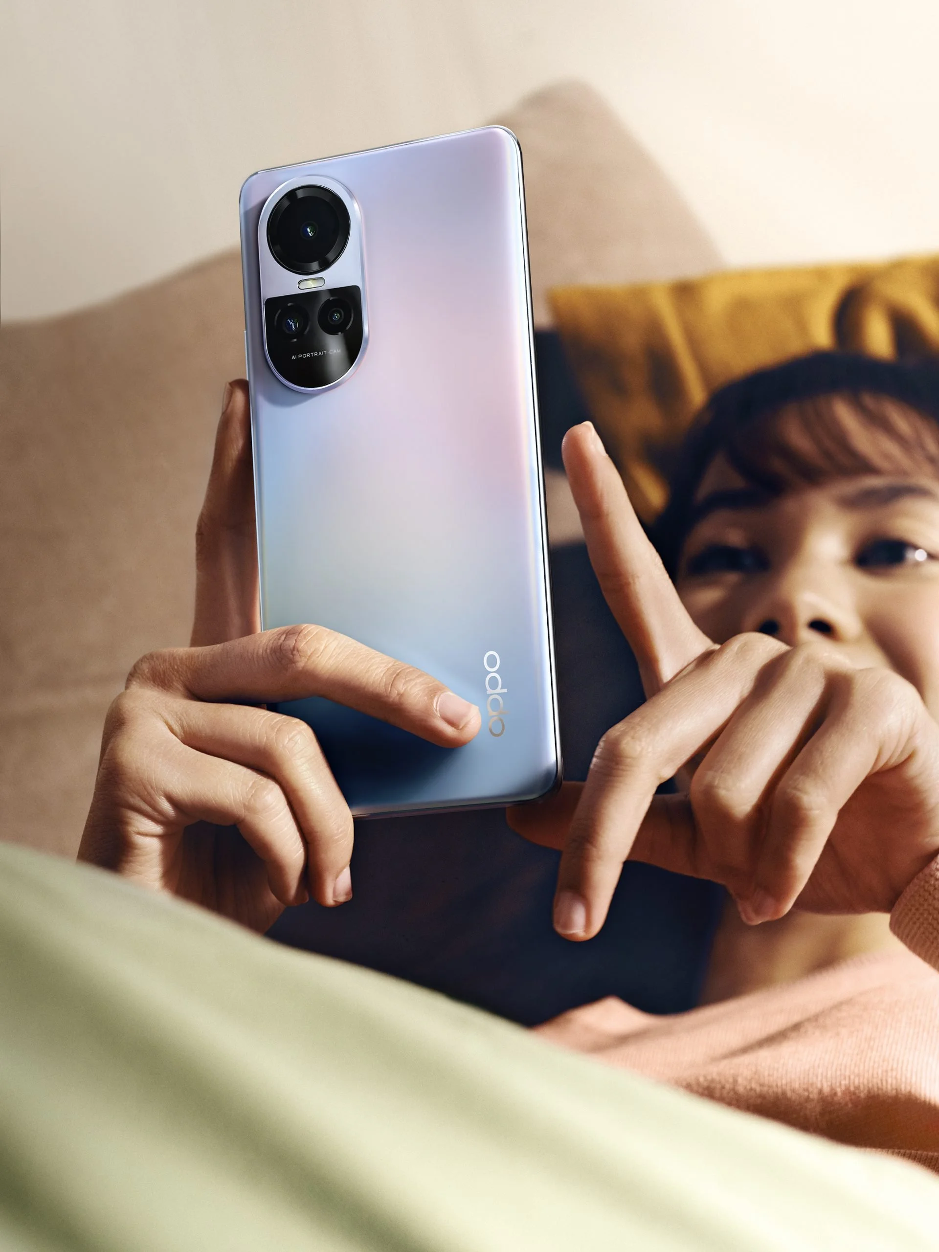 Close-up of a person holding a light-colored smartphone, with the brand name 'OPPO' visible, while another person is taking a selfie or recording a video.