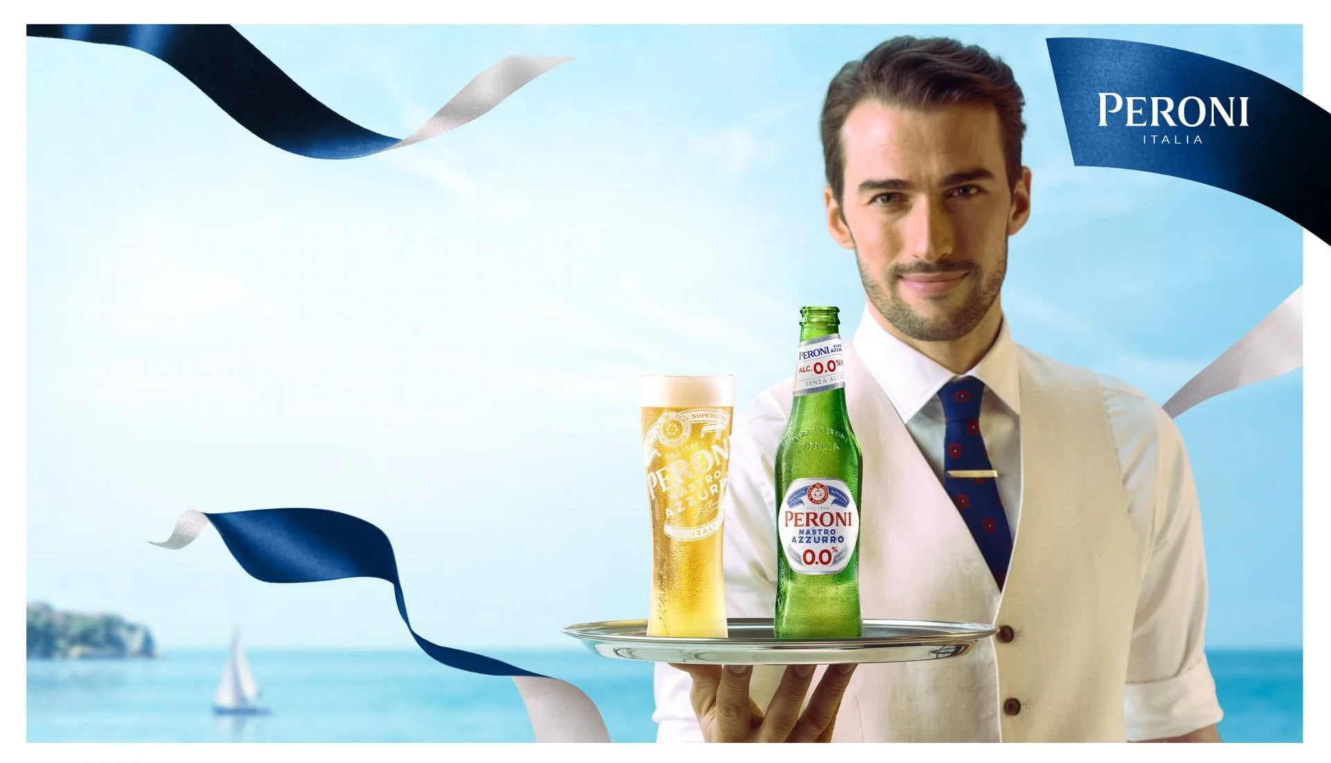 A man in a white shirt, vest, and tie holding a tray with a bottle of Peroni beer and a glass of beer, against a blue sky background with sailboats and floating ribbons, advertising Peroni beer.