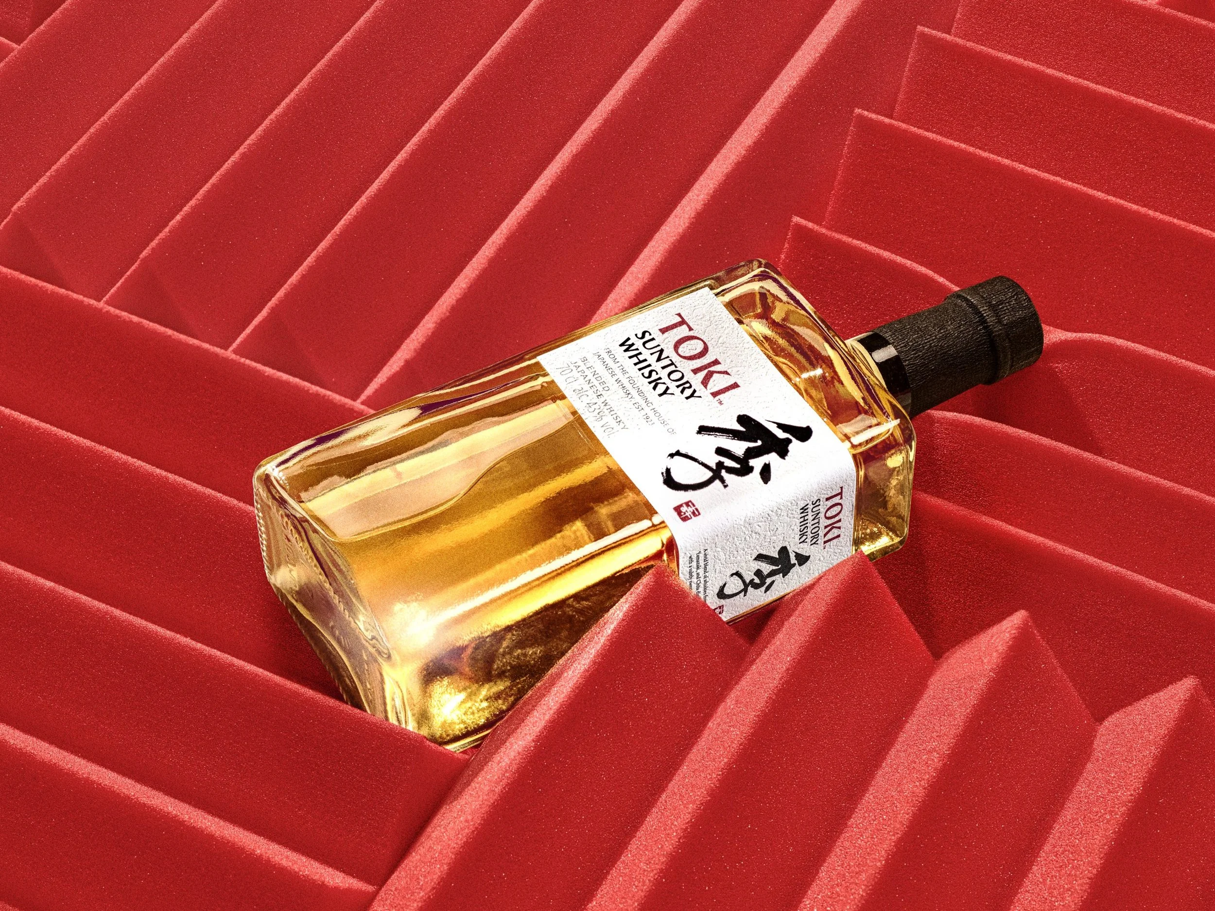 A bottle of Tokiji Suntory Whisky lying across a red, padded cardboard display box.