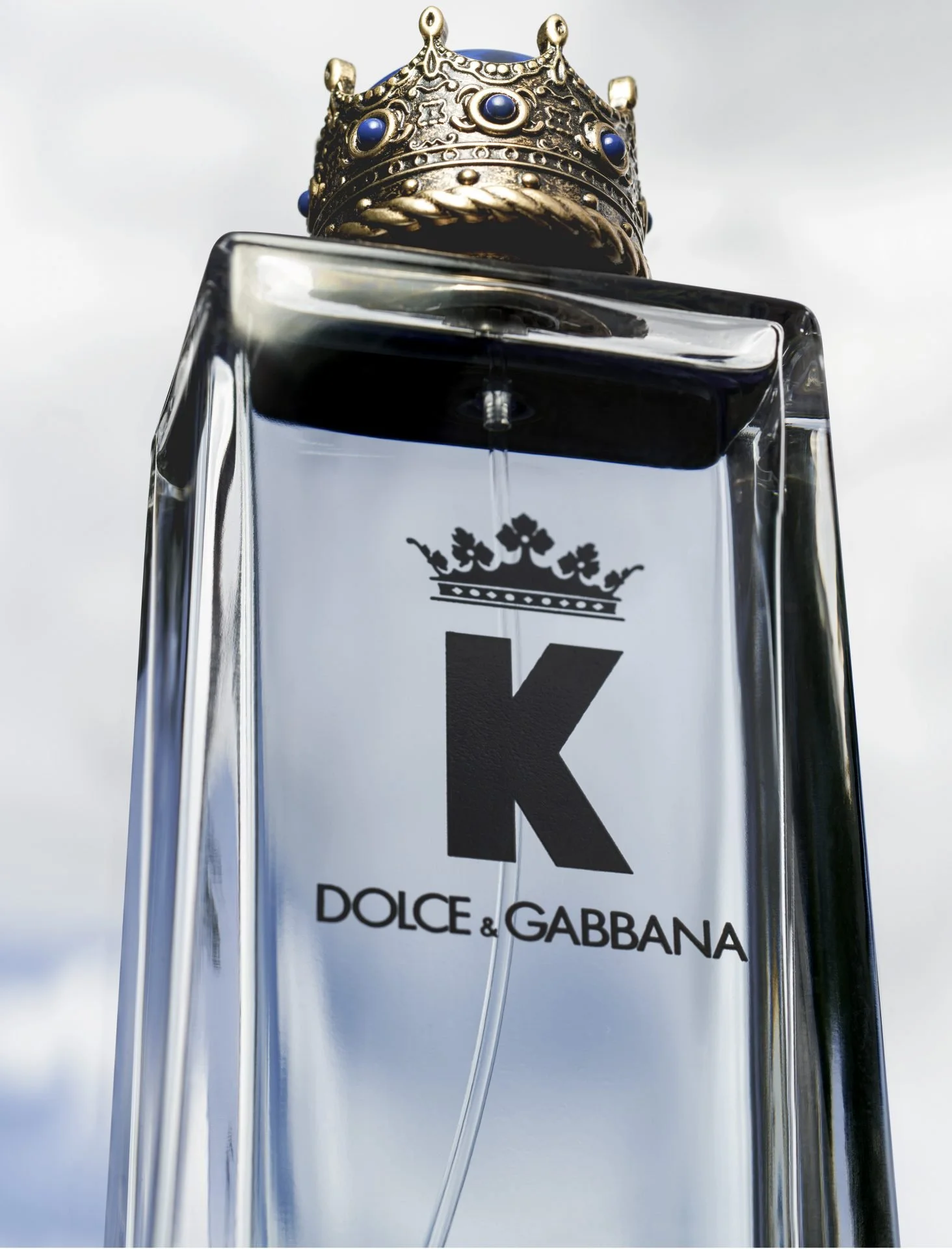 Close-up of a perfume bottle with the label "K" and the brand name "DOLCE & GABBANA," topped with a gold crown adorned with blue stones.