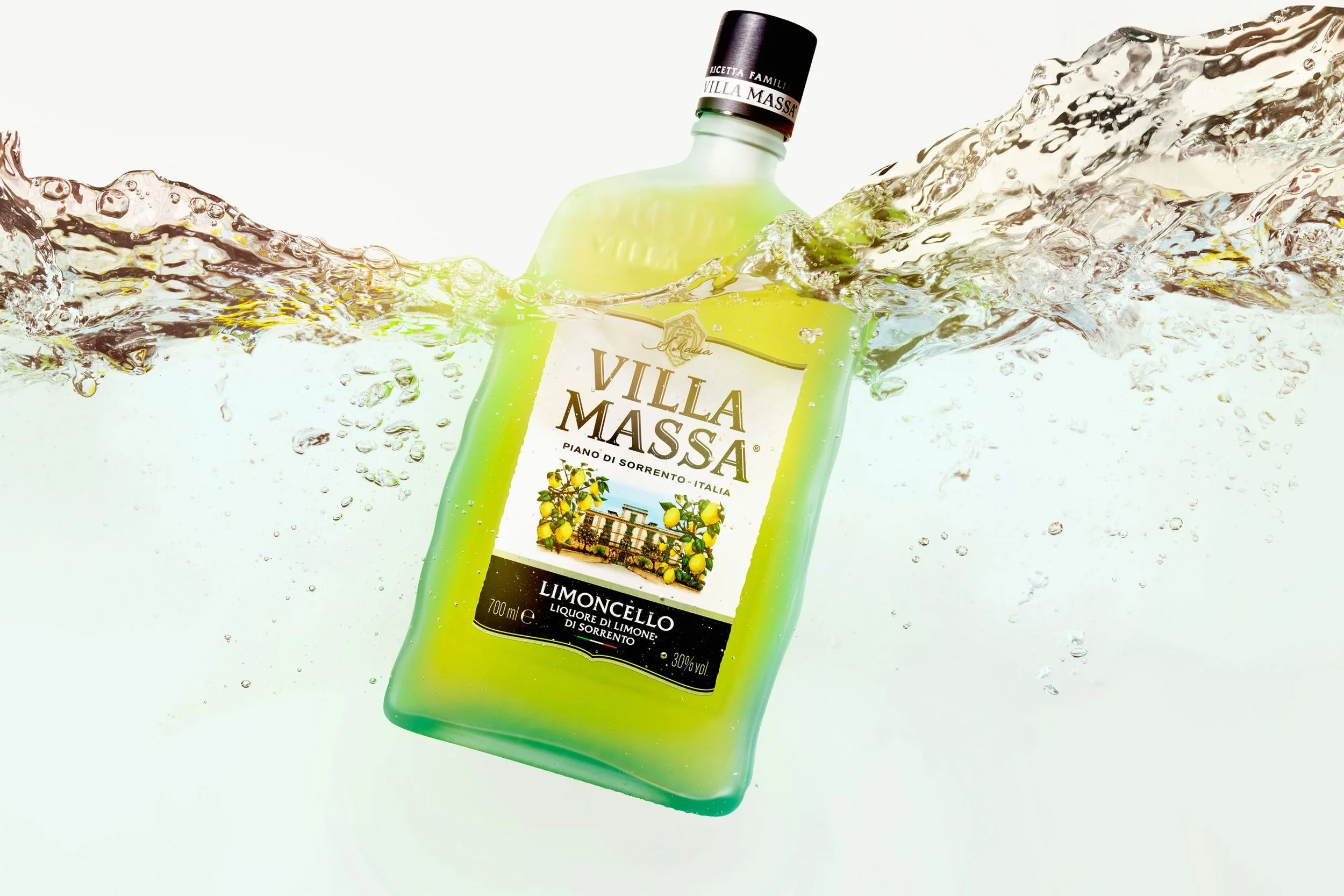 A green bottle of Villa Messa Limoncello liquor partially submerged in water with splashes around it.