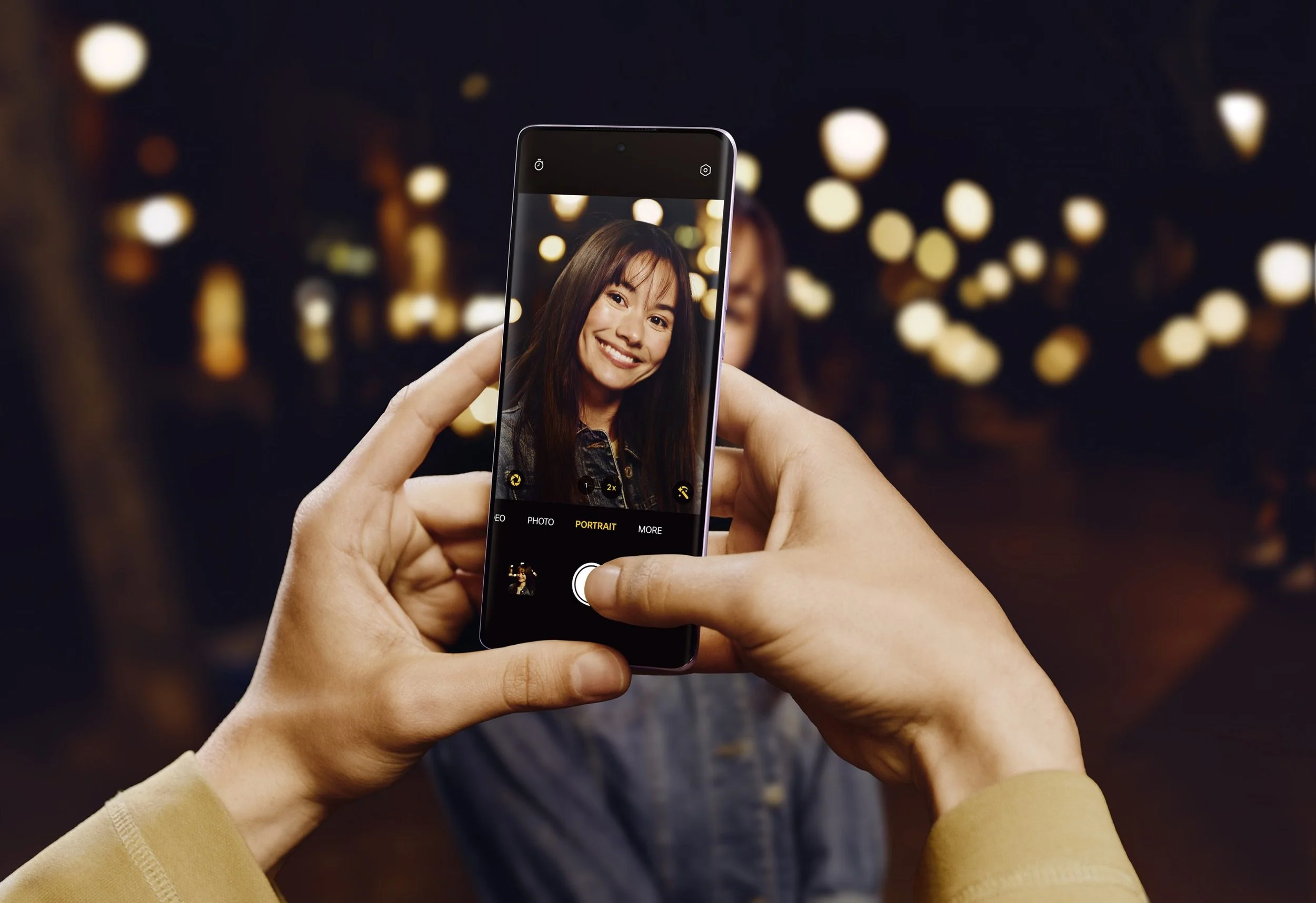 Person taking a photo of a woman with a smartphone in a dark setting with blurred lights in the background.