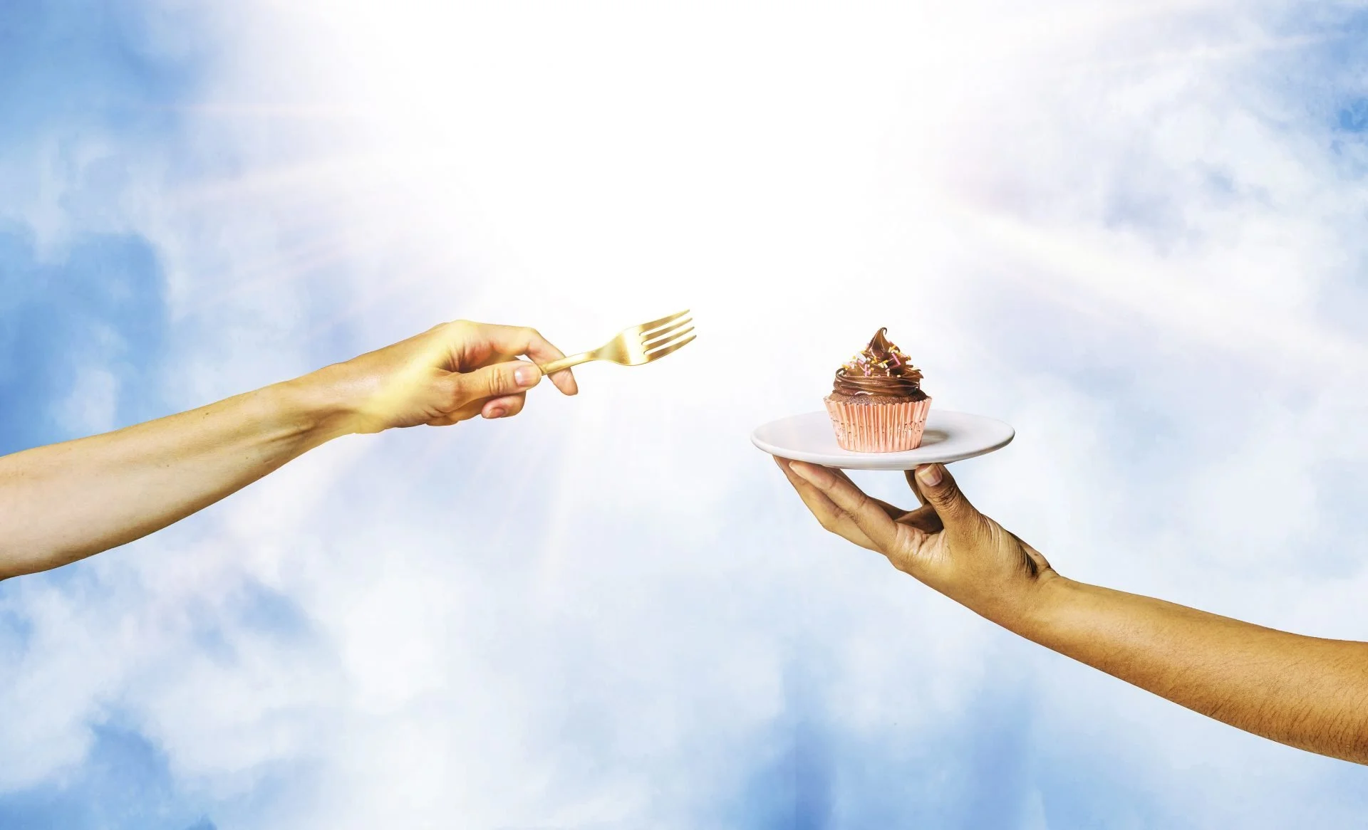 Two hands holding a cupcake on a plate, while a third hand extends a fork towards it, against a sky background.