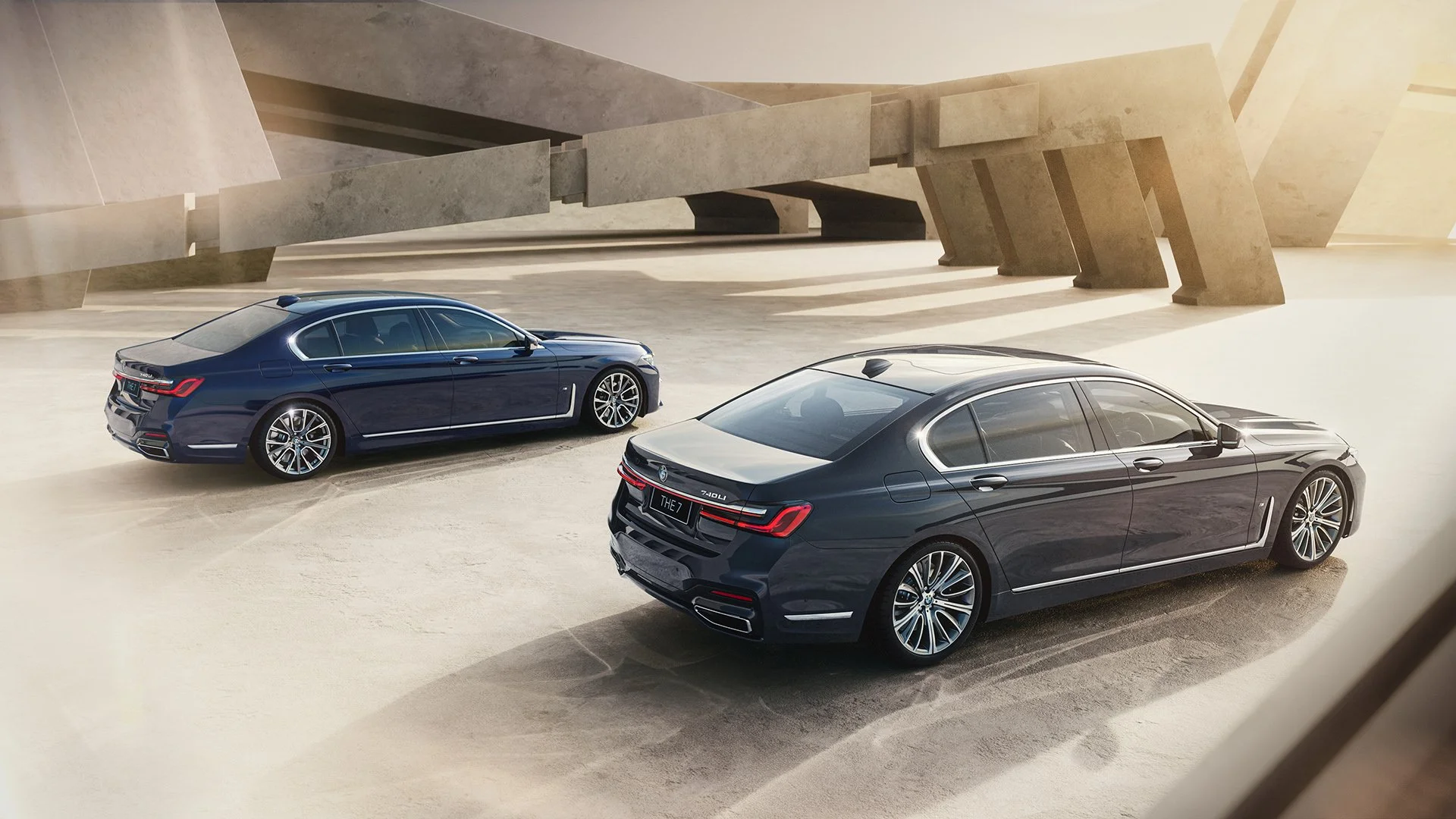 Two black sedans parked in an open area with modern architectural structures and a warm sunlight glow.