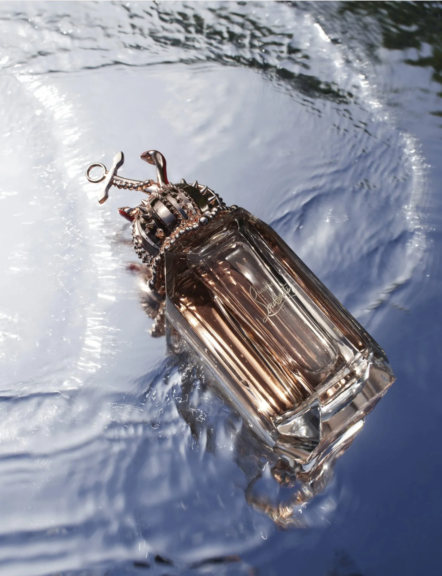 A perfume bottle with a crown-shaped topper is floating on water, creating ripples around it.