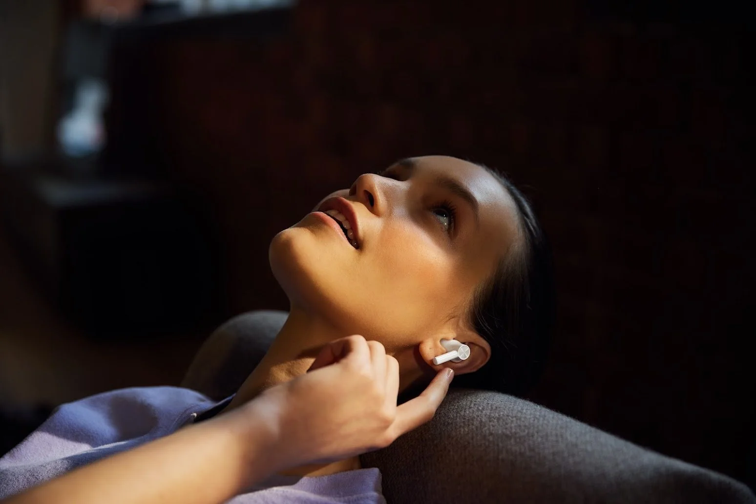 A woman reclining with her head tilted back, listening to music through wireless earbuds