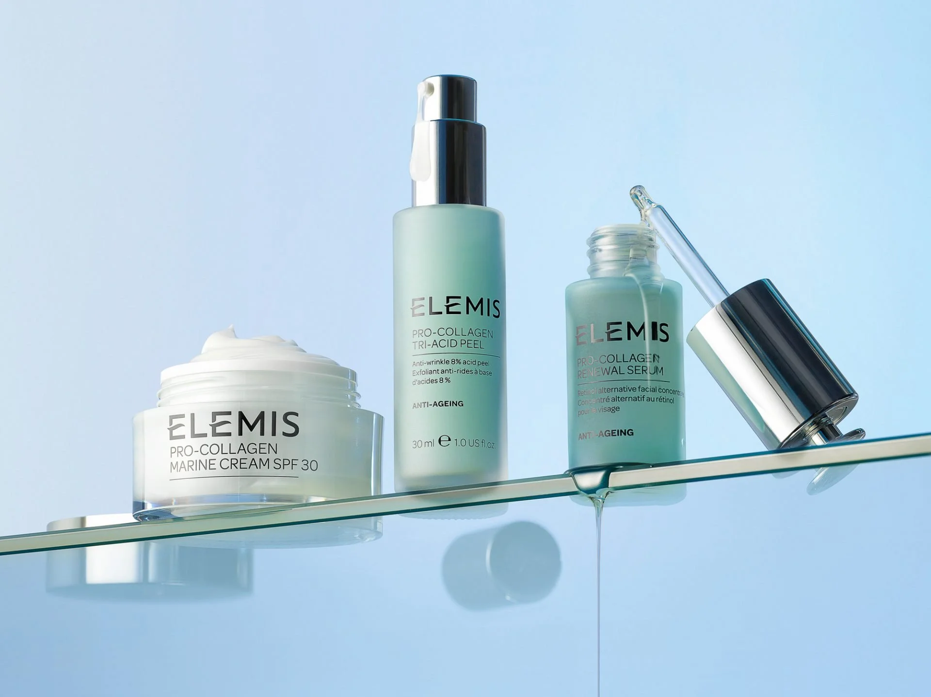 Skincare products including a jar of Elemis Pro-Collagen Marine Cream SPF 30, a bottle of Elemis Pro-Collagen Tri-Acid Peel, and a serum dropper on a glass shelf against a light blue background.