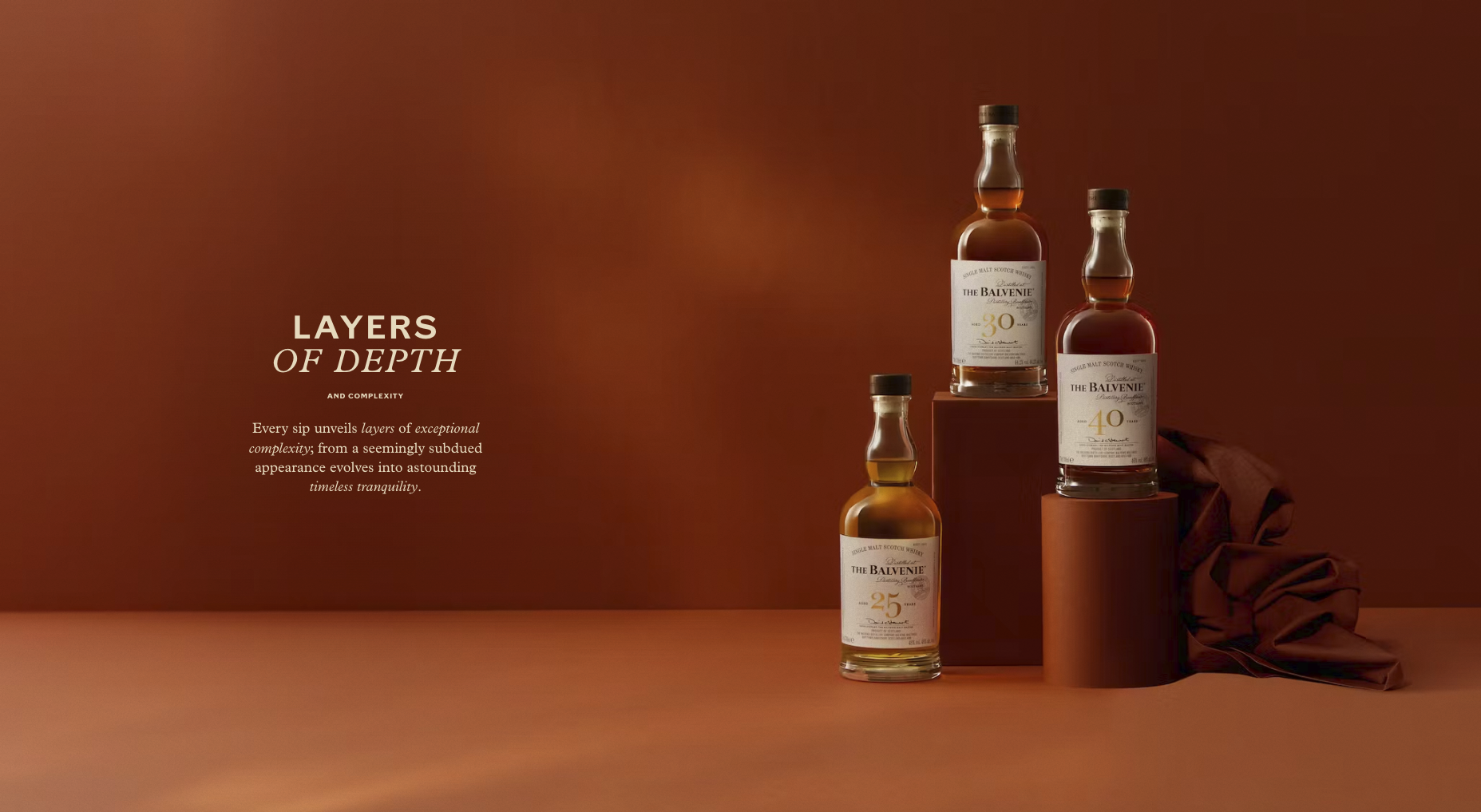 Three bottles of The Balvenie single malt scotch whisky, labeled with ages 25, 30, and 40, arranged on a series of cylindrical platforms against a warm brown background. Text on the left discusses layers of depth and complexity.