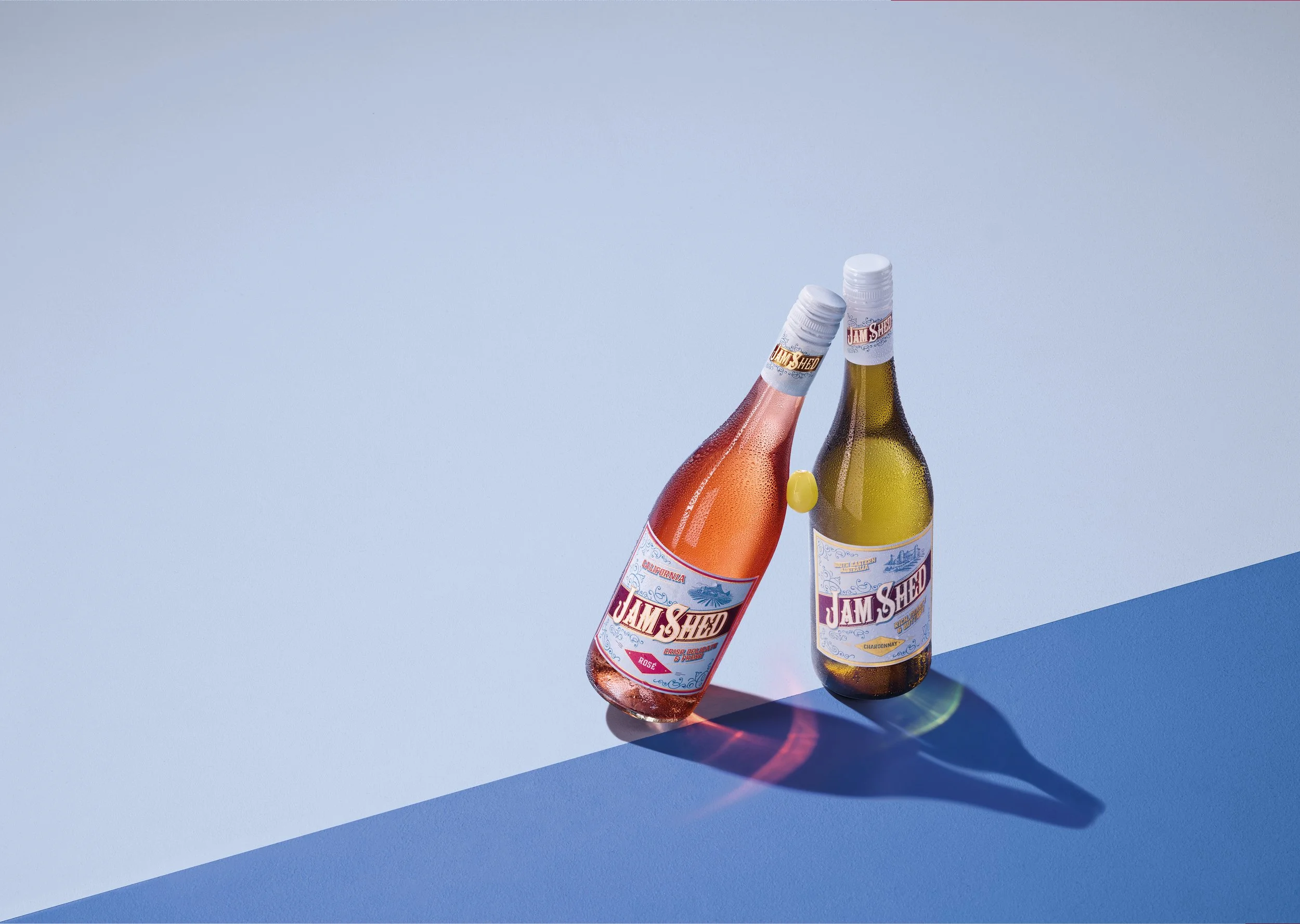 Two bottles of Jam Shed sparkling wine, one rosé and one Chardonnay, placed on a light blue surface with a white background.