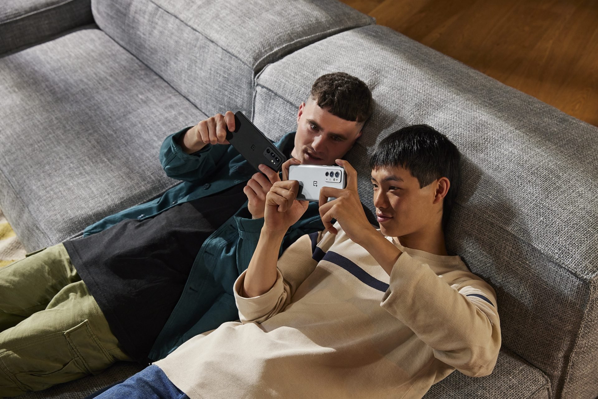 Two young men lying on a couch, viewing their smartphones
