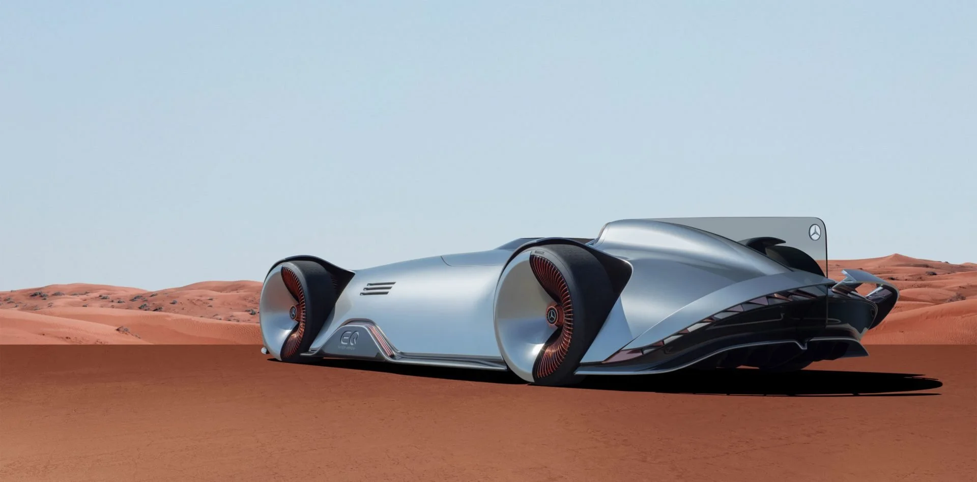 A futuristic silver concept car with streamlined design and large side air intakes, situated on a desert landscape with red sand dunes and a clear blue sky.